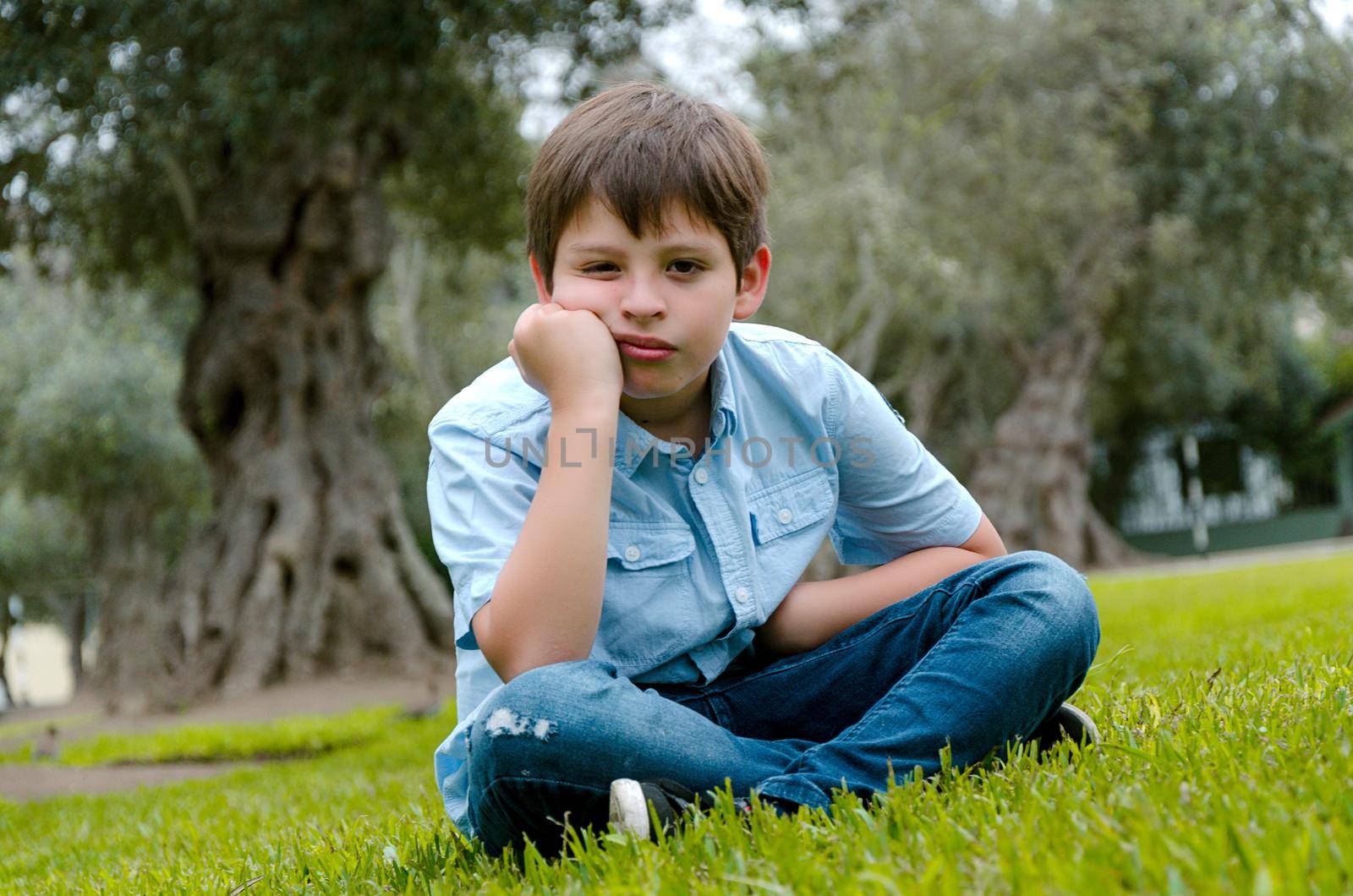 Toddler boy with funny face sad or bored .he sitting alone at park on autumn day