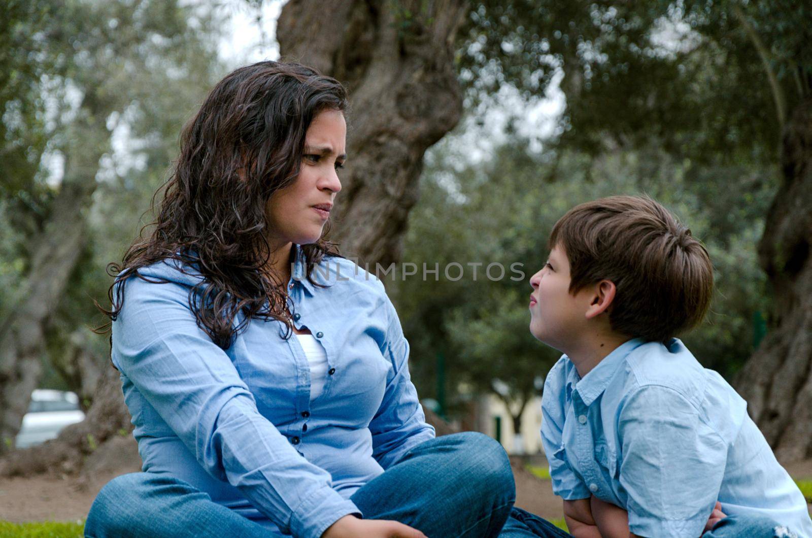 Portrait of a mother scolding to her son sitting on the grass by Peruphotoart