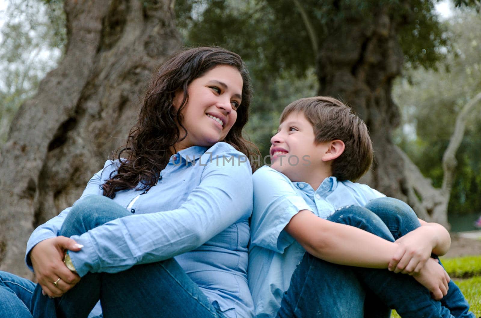 Mom and son sitting on green grass in green park. Concept of happy family relations and carefree leisure time