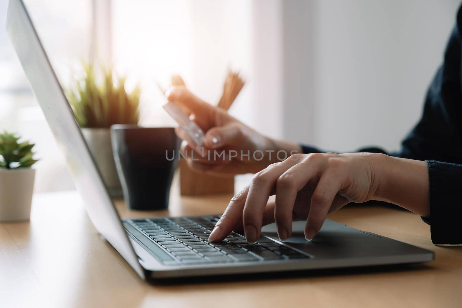 Close up hand of woman holding credit card and using laptop computer at home. Online shopping, e-commerce, internet banking, spending money