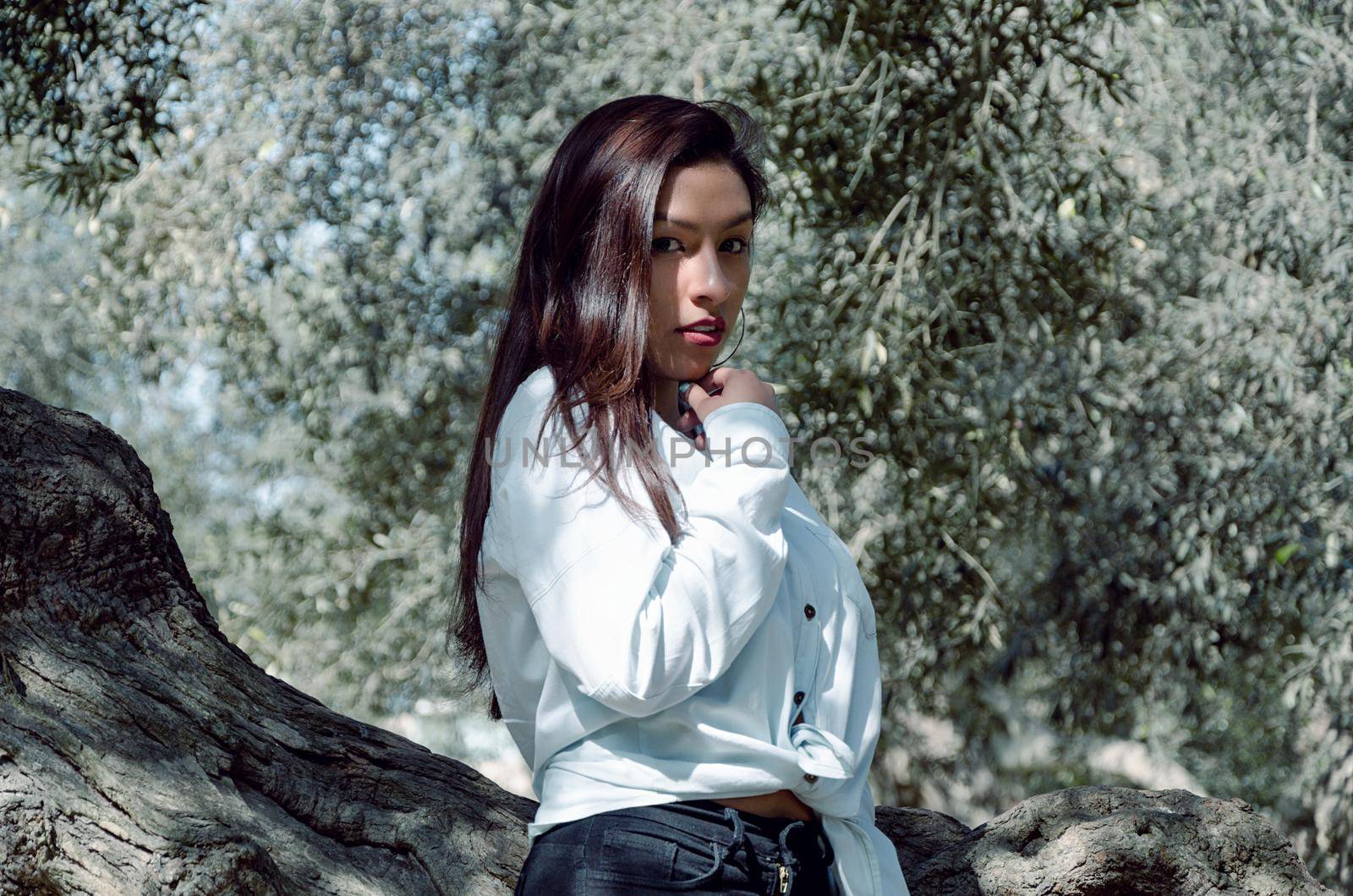 Beautiful young brunette woman leaning on the tree in the park