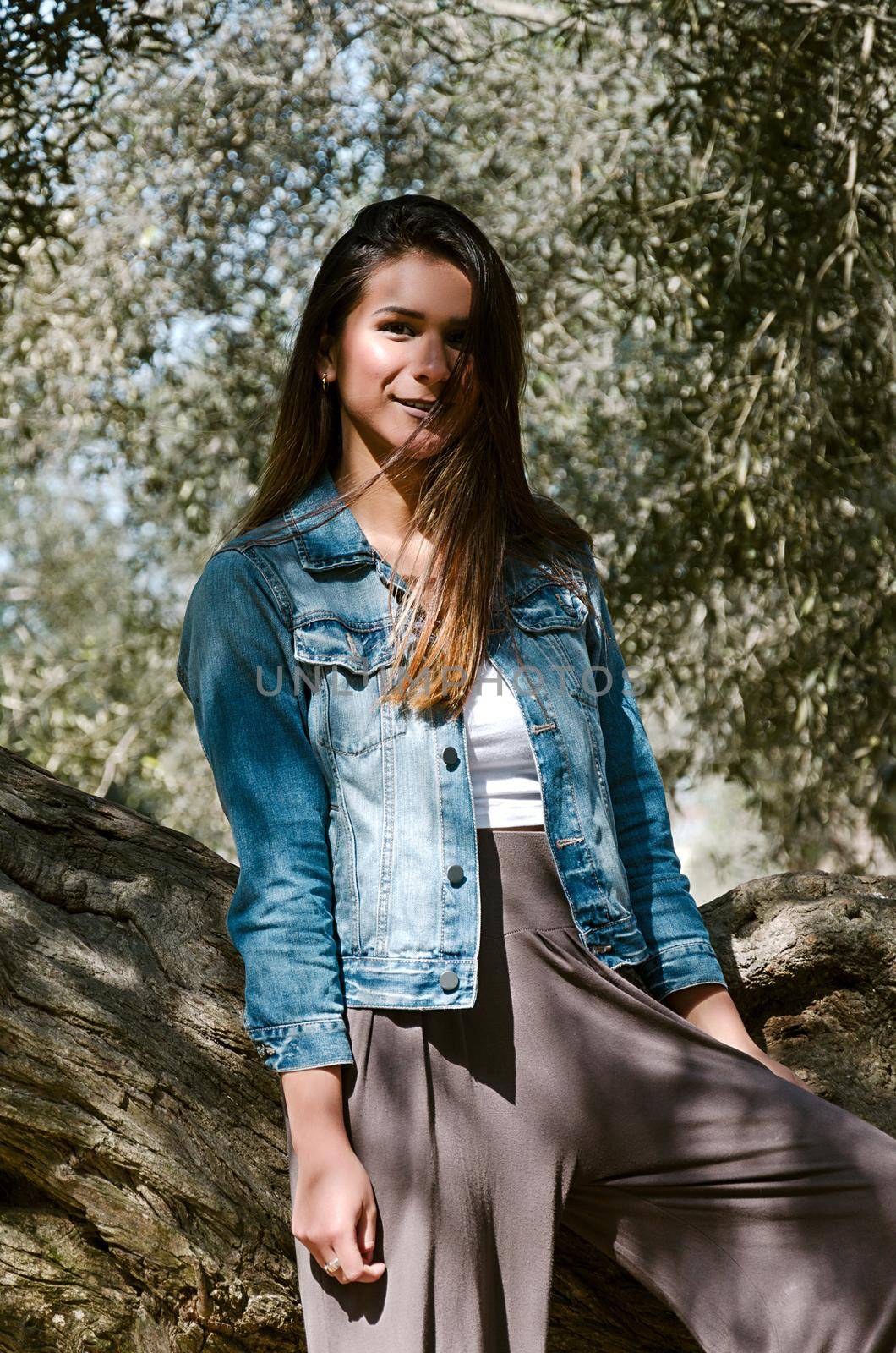 Beautiful long-haired teen woman with brown hair leaning on a tree in the park