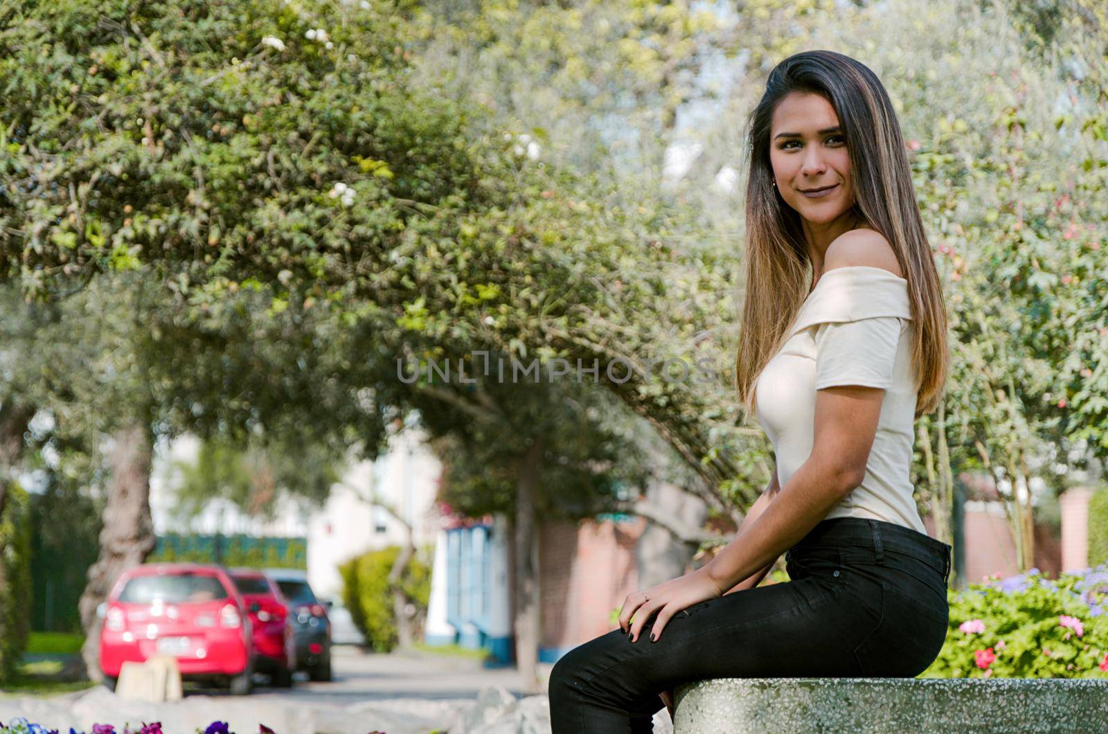 Happy young woman sitting on bench in city park Stylish fashion model wearing ripped jeans and pullover