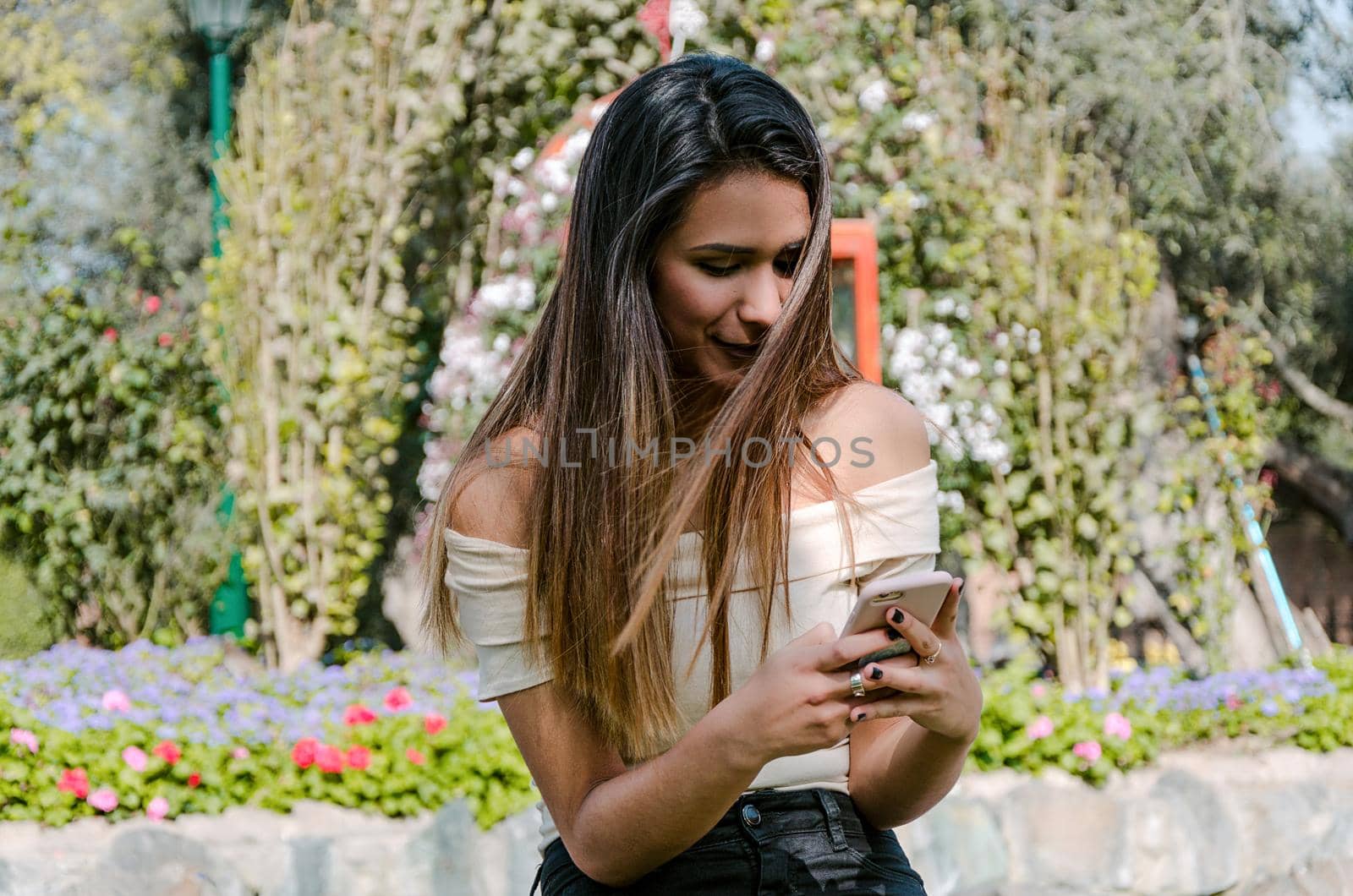 Happy girl watching media in a smartphone sitting on a bench of a city park