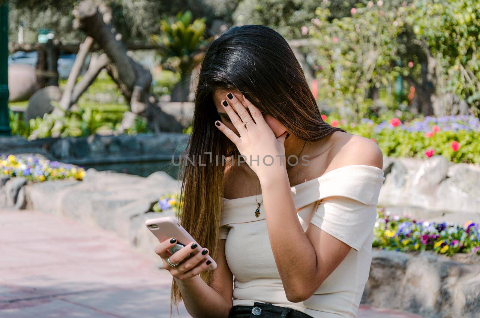 Worried Hipster teenager girl looking at her smart phone in a park with an unfocused background