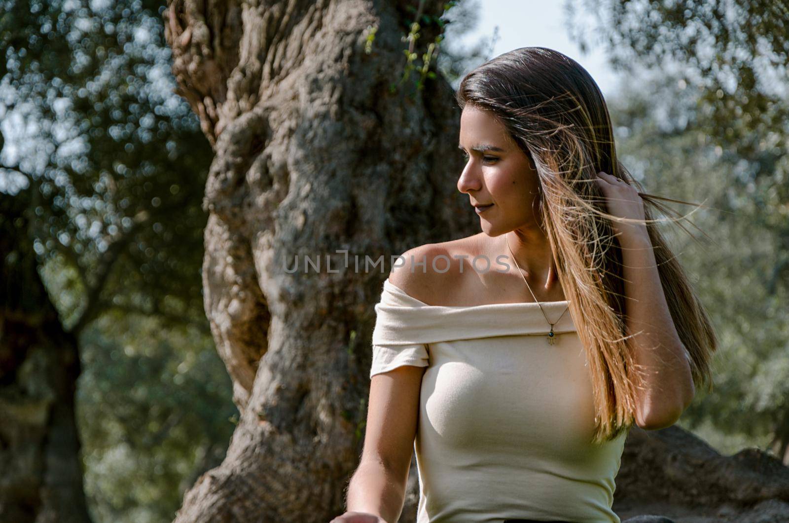 Beautiful brunette woman touching her long hair. She sits in a park on green grass. The image is toned.