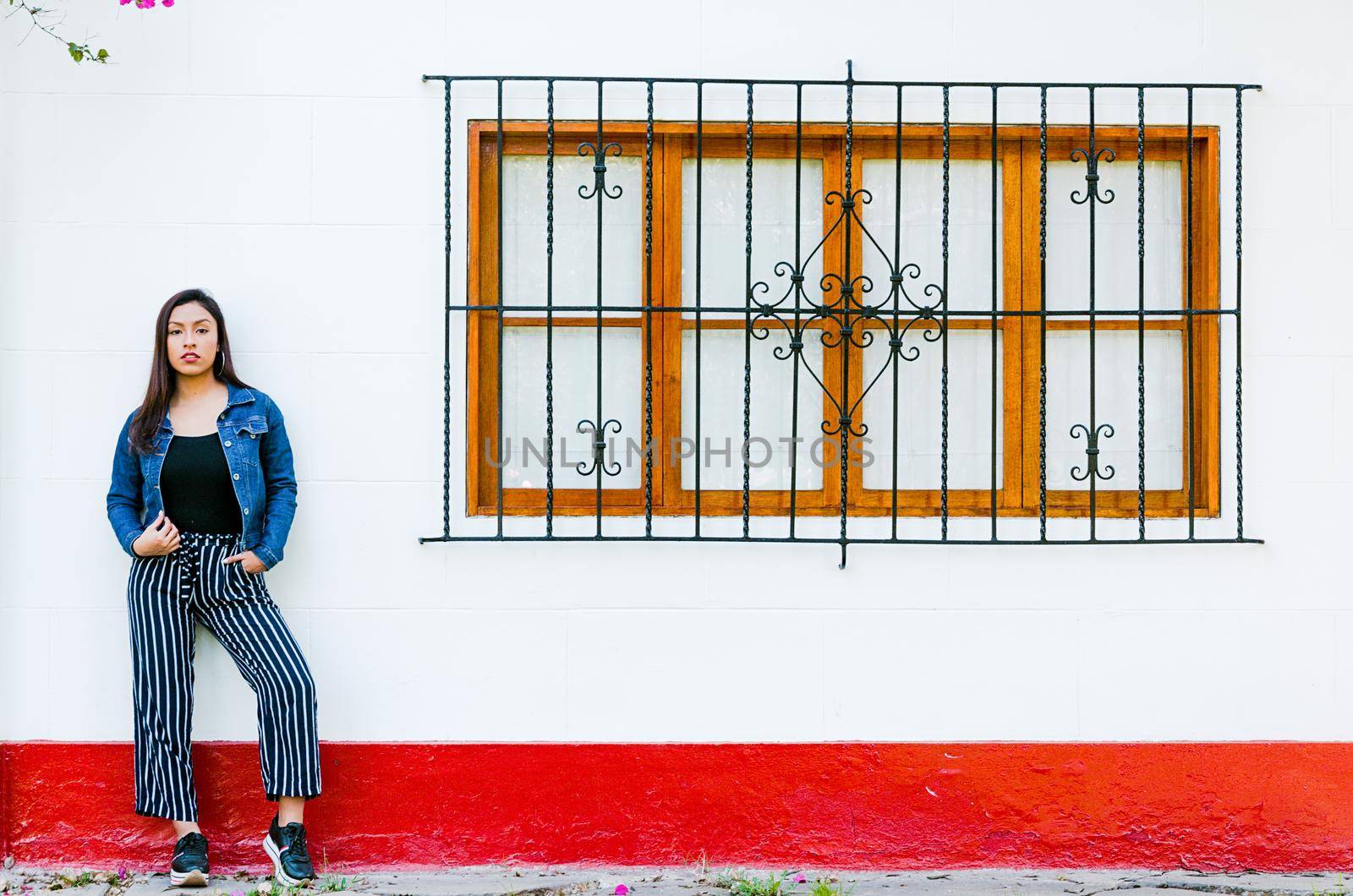 Stylish young woman posing against window outdoors. Fashionable outfit. Beautiful model smiling