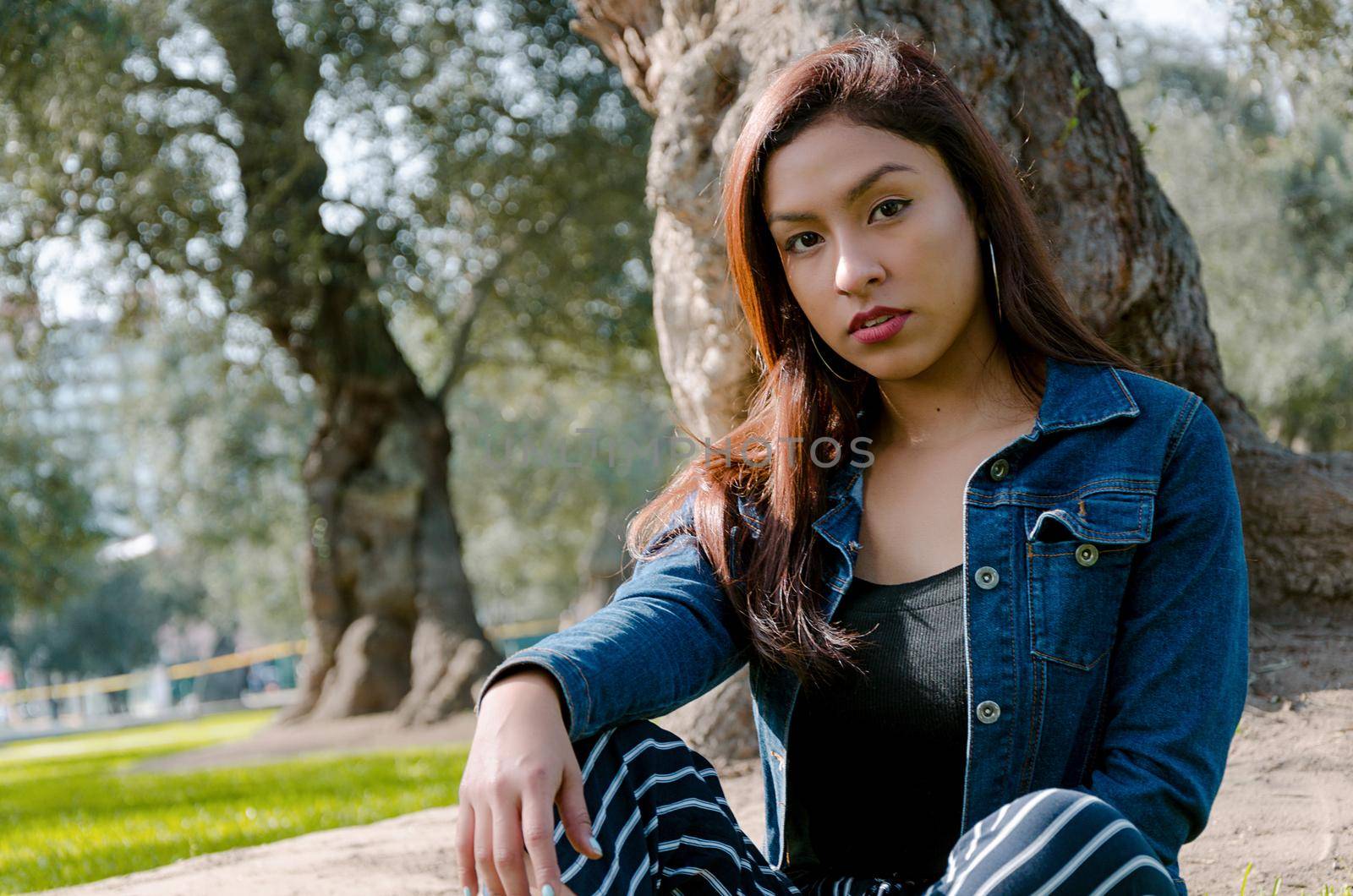 Portrait of an attractive, young and attractive brunette woman sitting on the lawn. She leans back and relaxes while smiling.