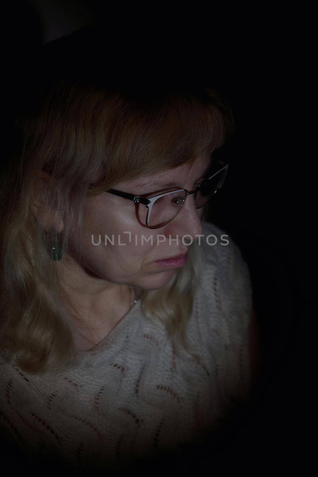 Face portrait of an aged woman wearing glasses with white long curly hair. Black background