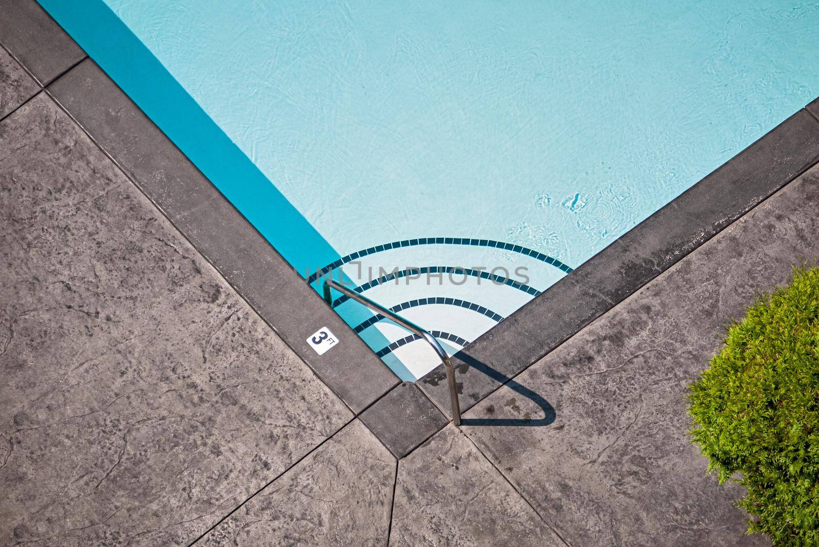 Corner of emerald swimming pool with steps leading to the deeper water and metal rail on side