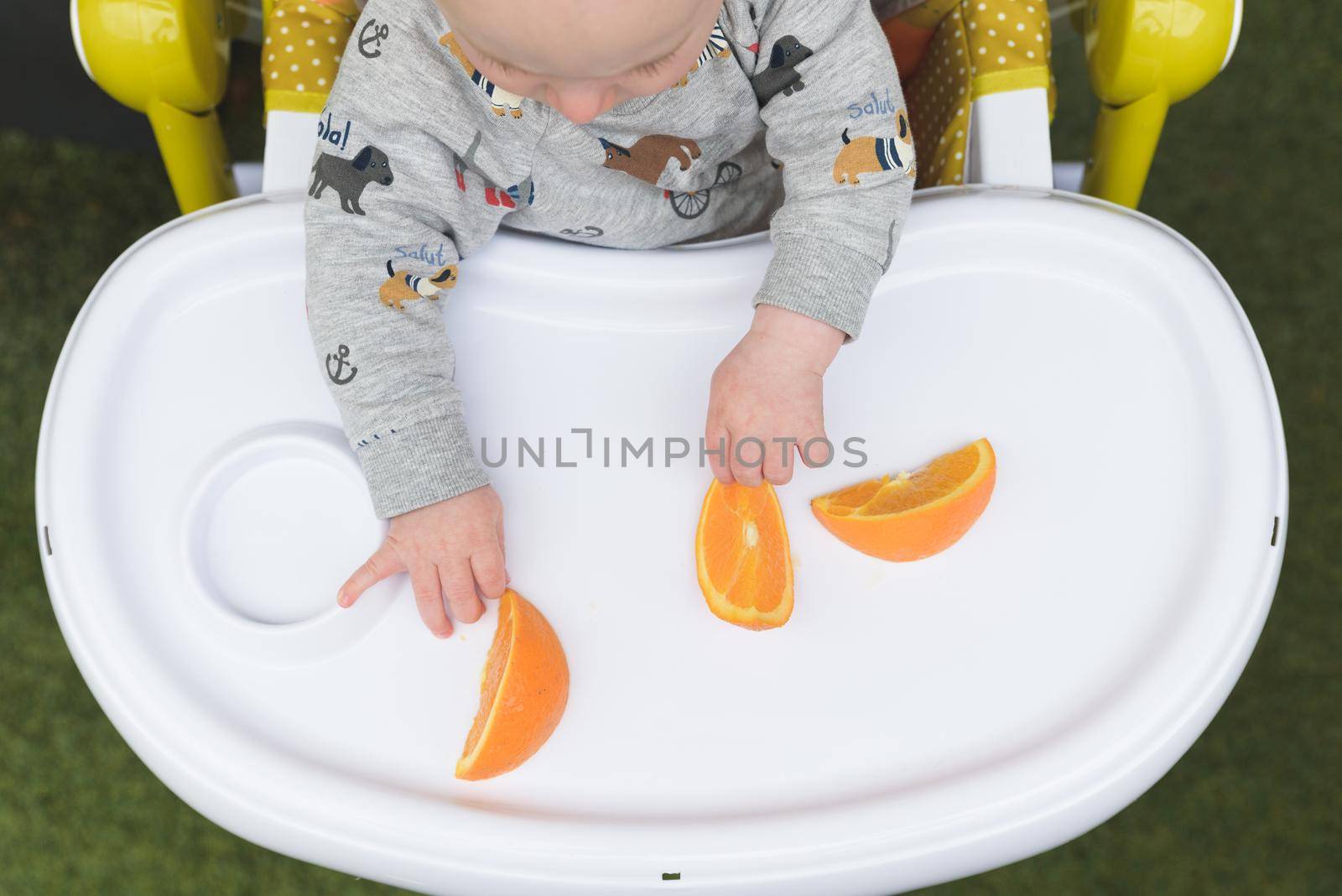 Cute little baby eating orange sitting in the high chair.