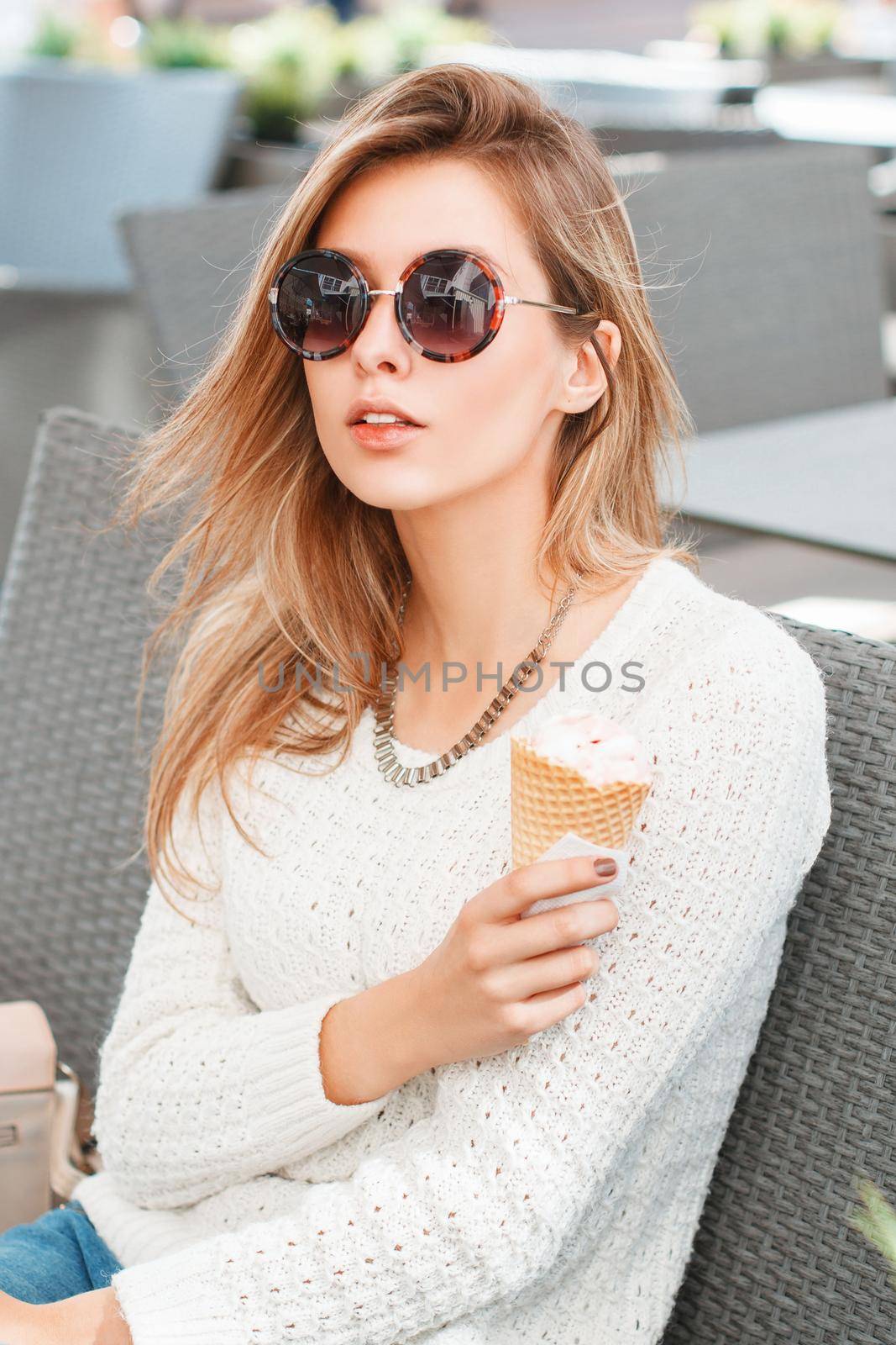 Fashionable beautiful girl in round sunglasses and ice cream sitting in a summer cafe.