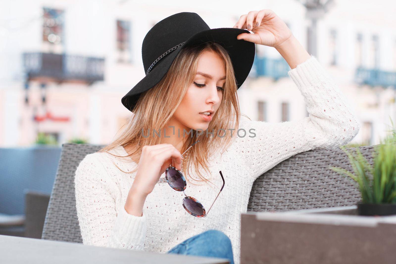 Beautiful stylish girl in a hat and sunglasses resting on a sunny day in a cafe by alones