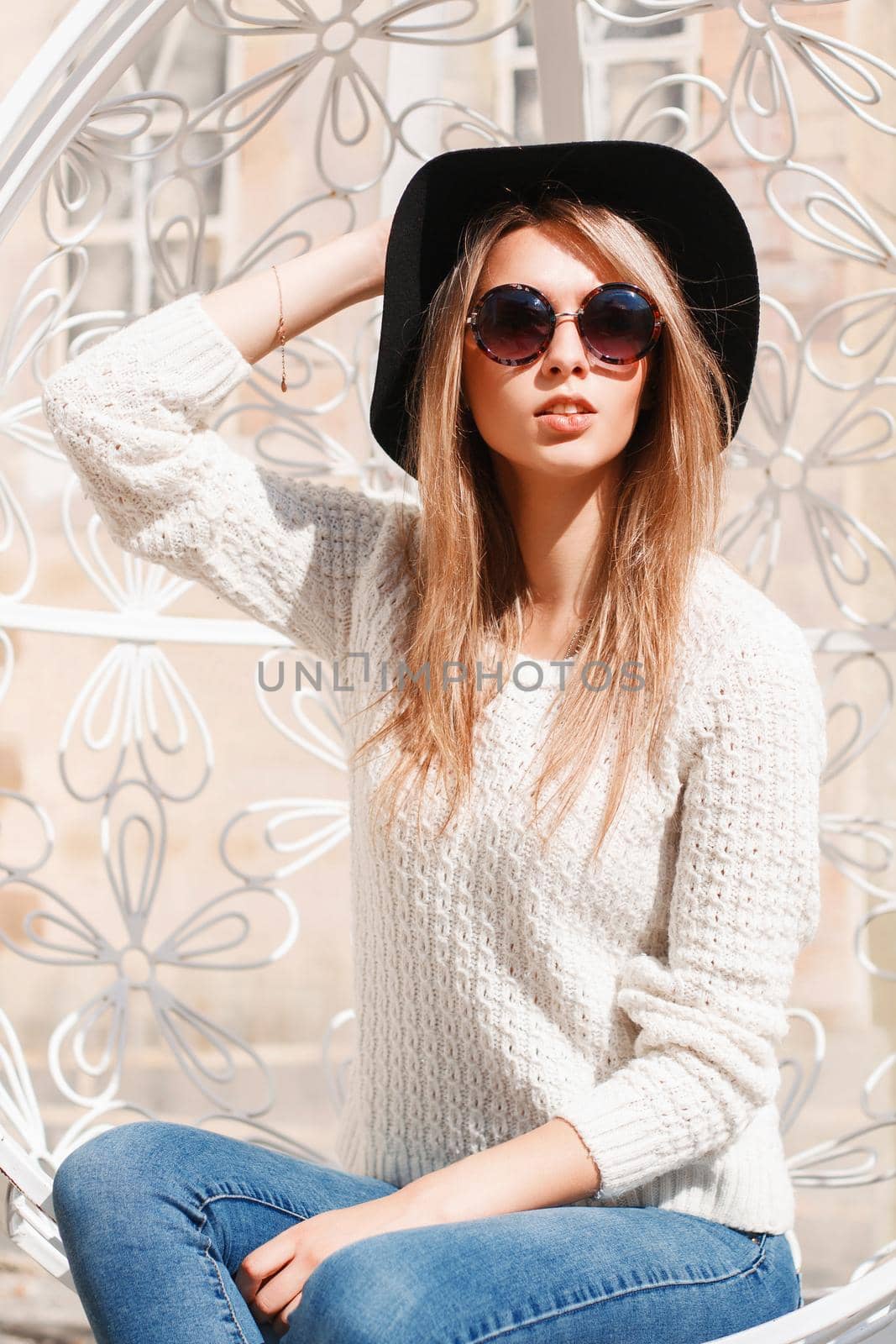 Pretty woman in a hat and sunglasses resting on a sunny day in a white suspended chair by alones