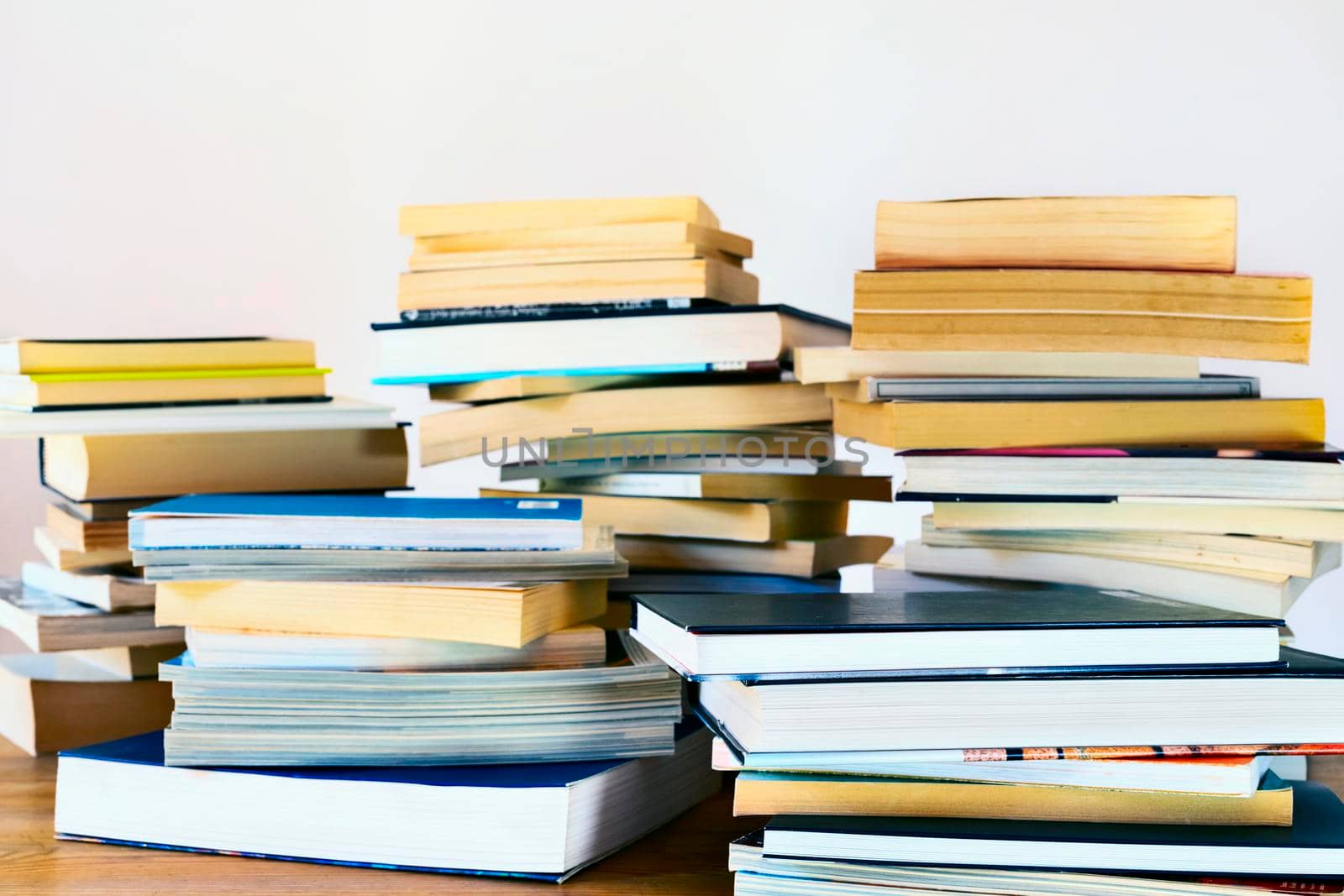 Several stacks of different books on a wooden table , books used and new ,