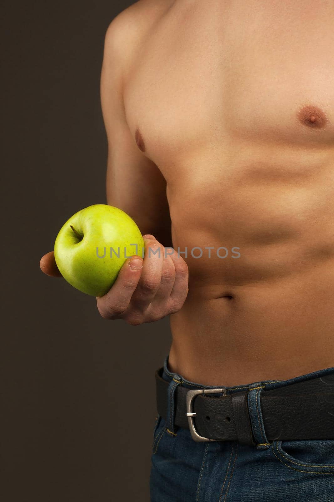 Man holding the apple. Abdominal muscles and chest. Athlete in the studio.