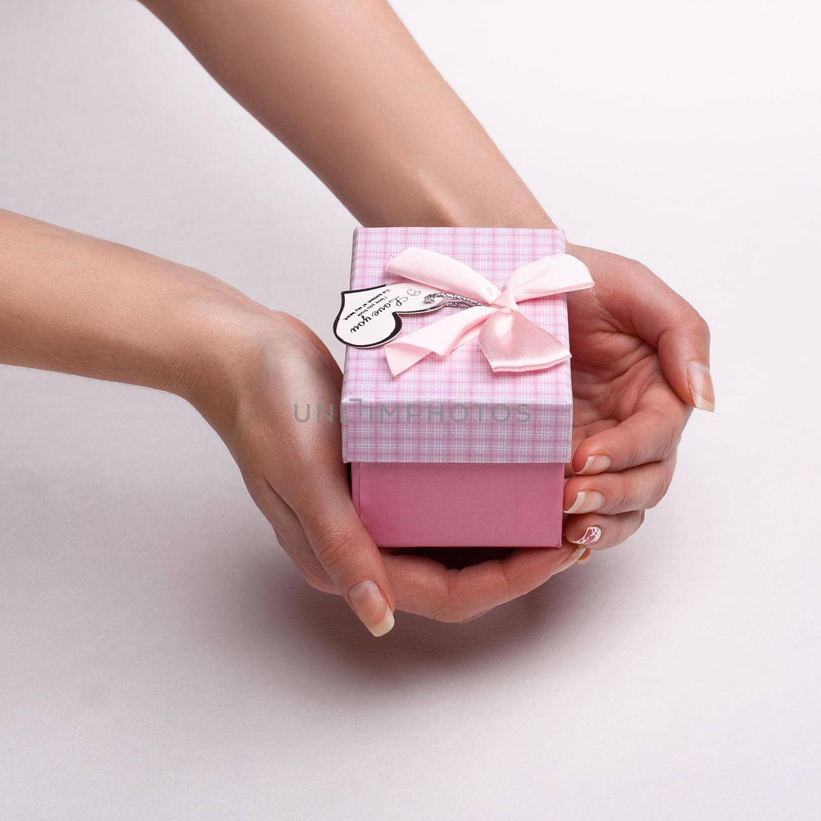 Women's hands holding a pink gift with a note I love you.