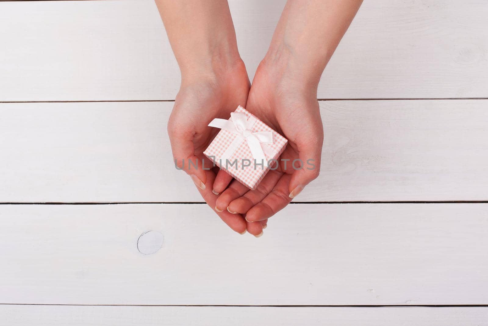 Female hand holding pink gift in hands on a white wooden table. View from the top.