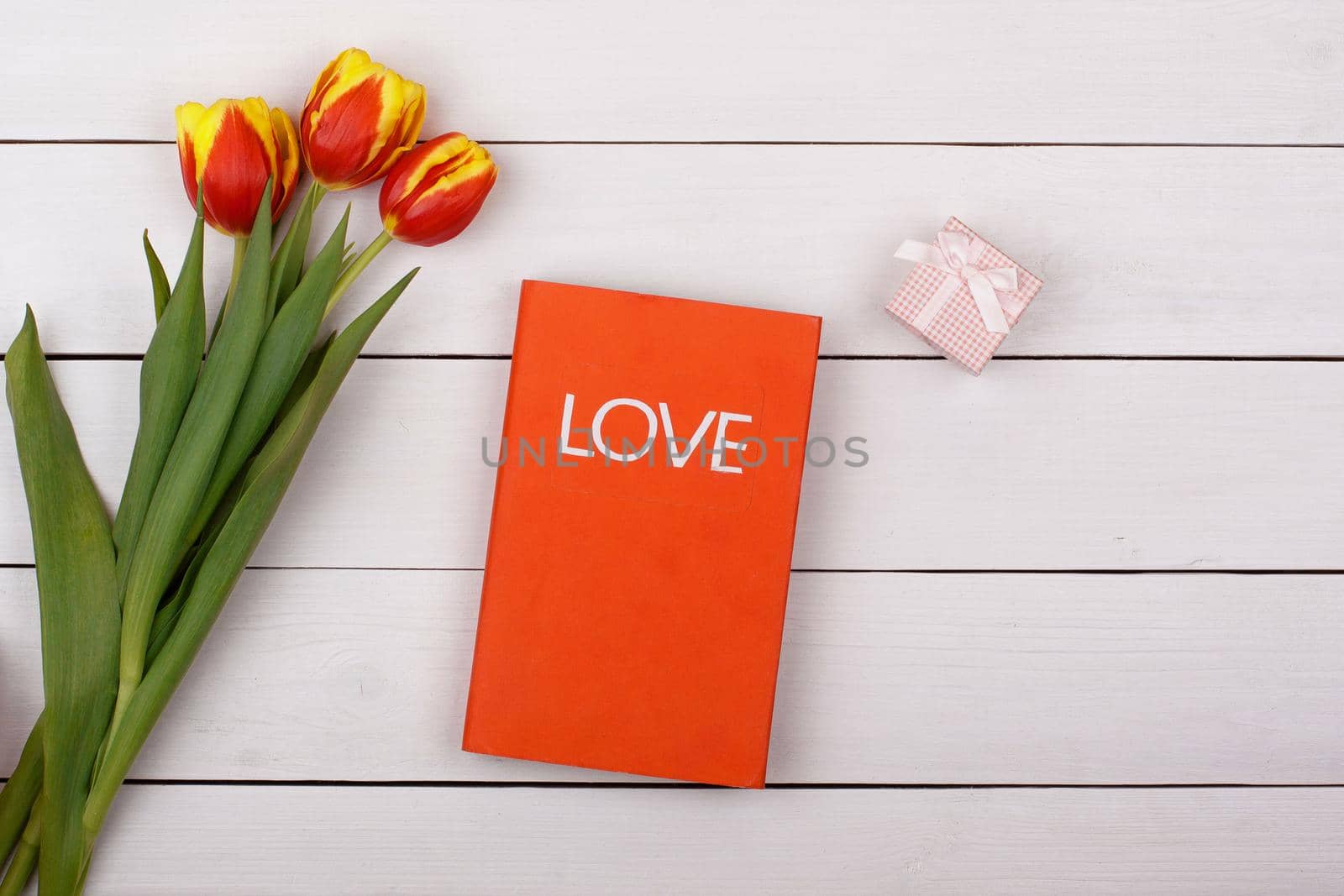 The red book Love lies on a white table. Flowers tulips and gift with a bow on the table. by alones