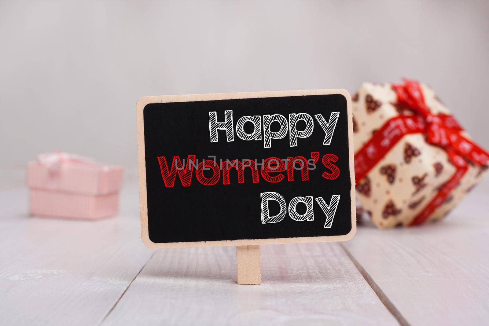 Happy Woman's Day message written on little chalkboar. Background with gifts.