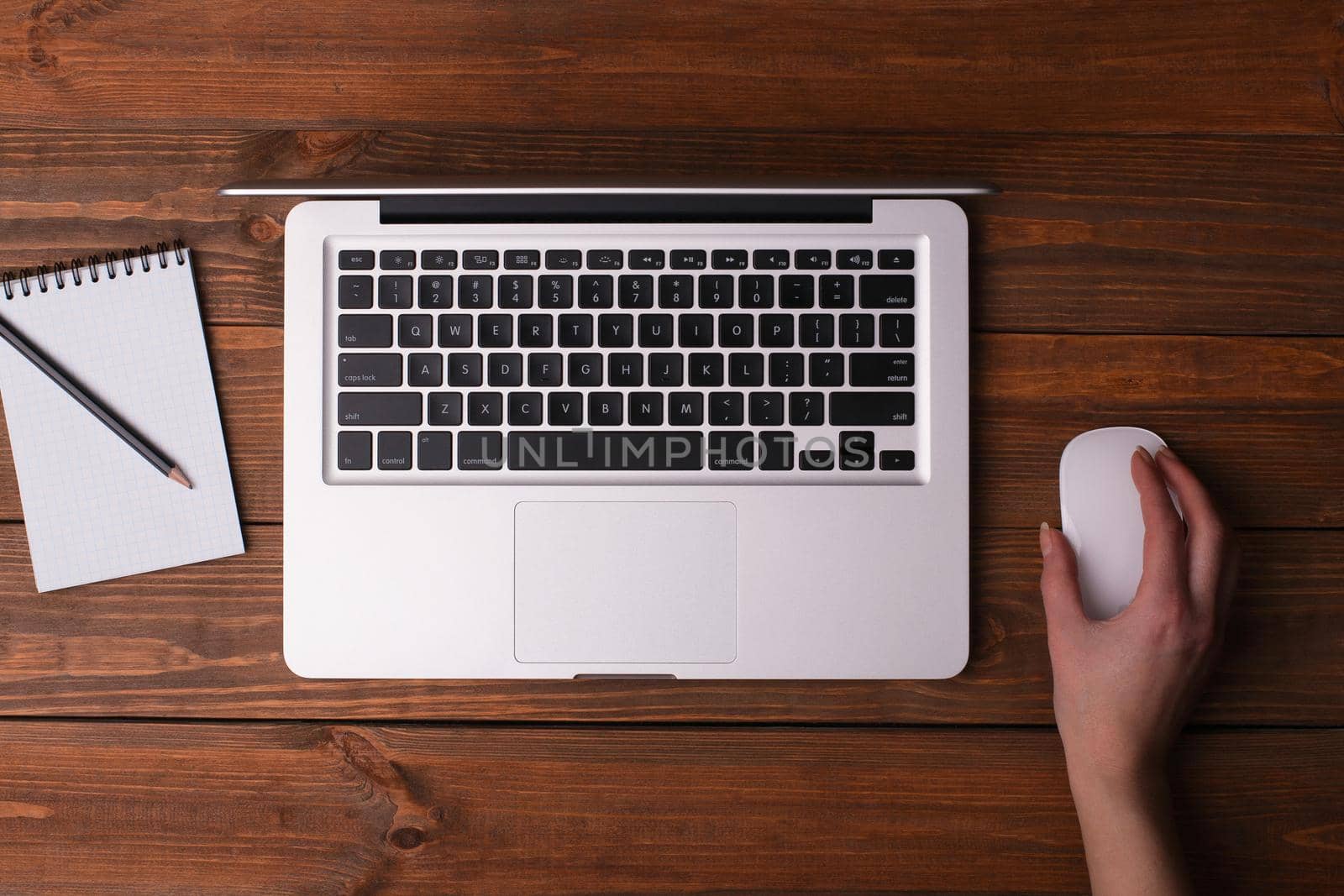 Desk with a laptop, a notebook with a pencil. Female hand holding a mouse.