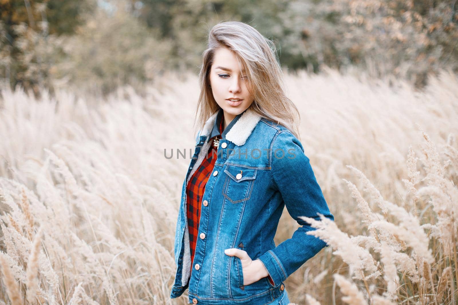 Young girl in jeans clothes and a red checkered shirt in the autumn field with grass by alones