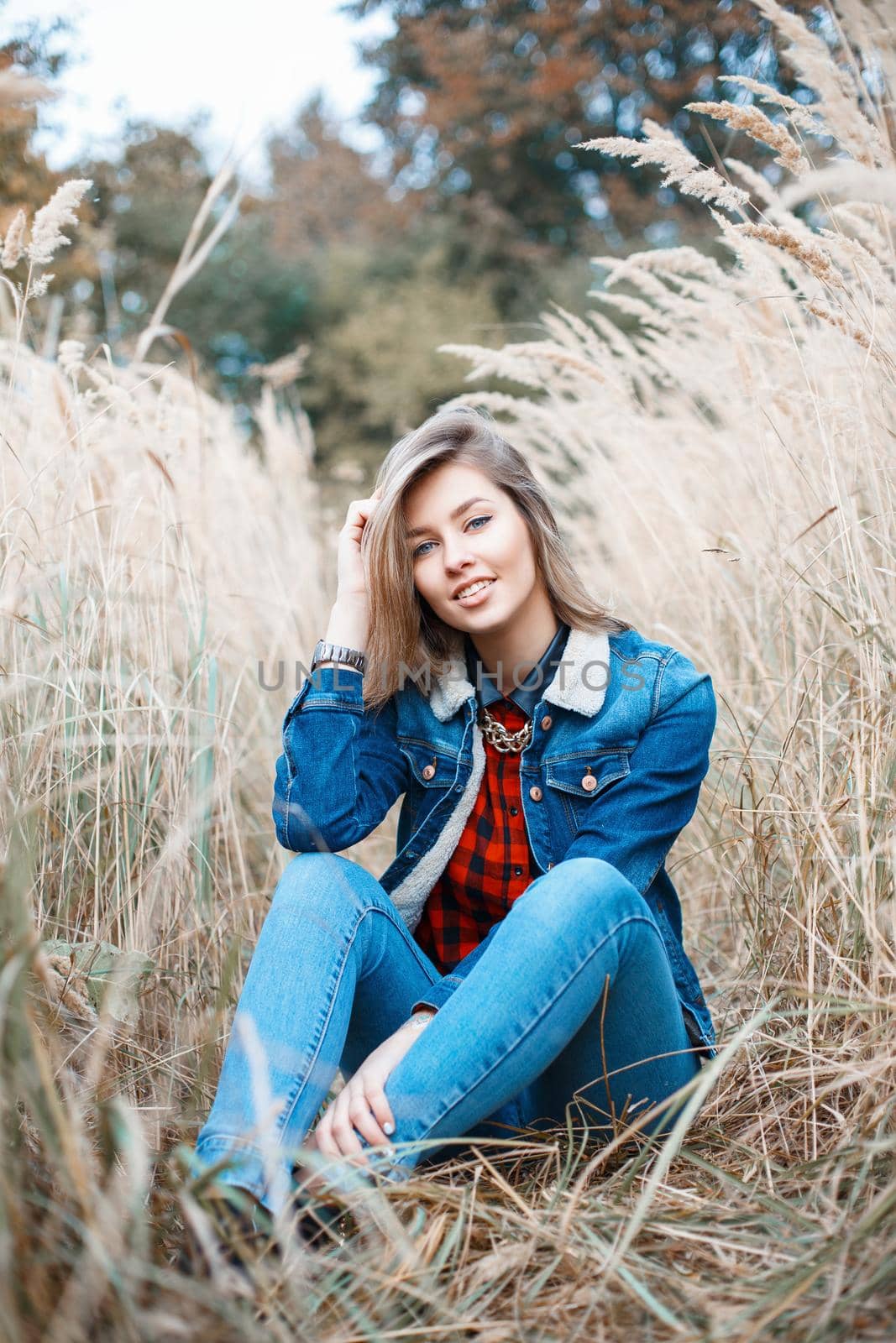 Beautiful positive girl in denim clothes sitting in autumn grass. by alones