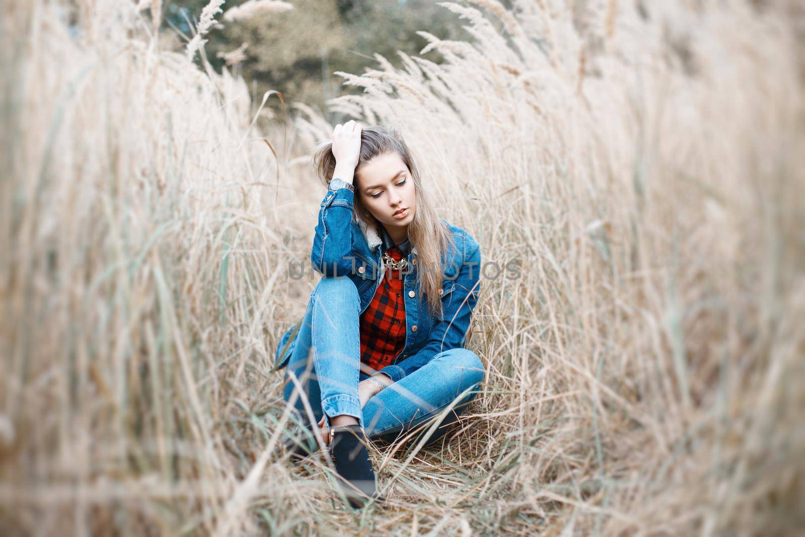 Pretty girl sits in a beautiful autumn grass. Blue jeanYoung beautiful girl with a smile in denim clothes. jacket. by alones
