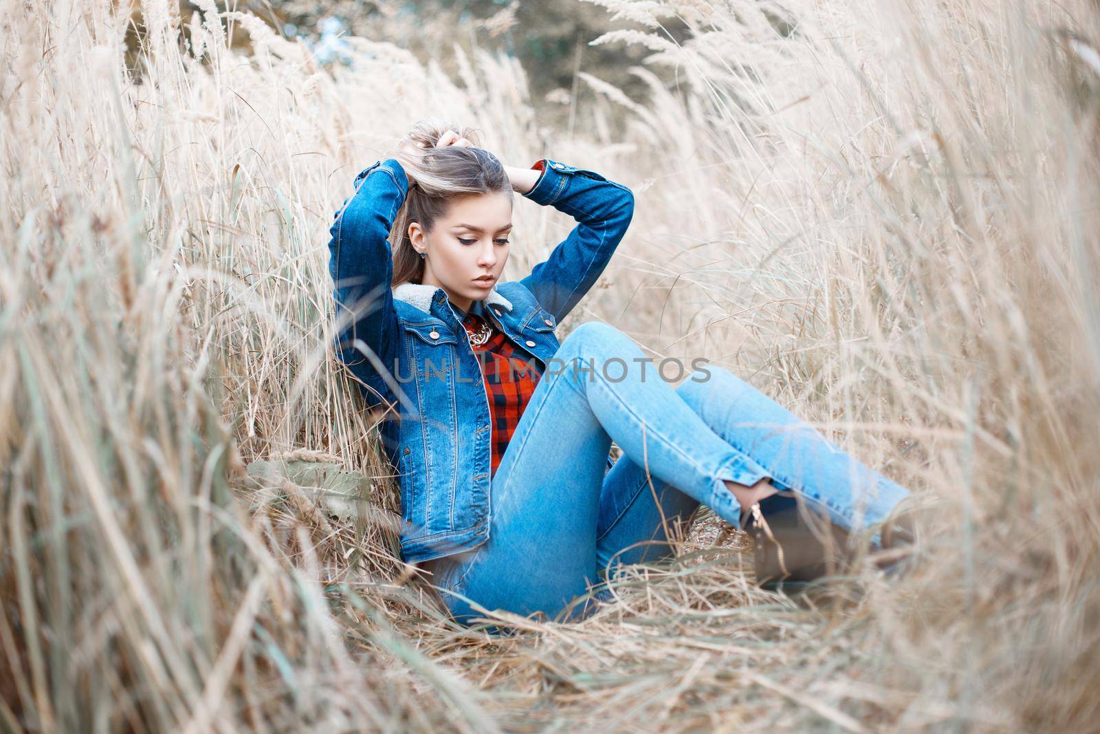 Pretty woman in a denim jacket and jeans sitting in autumn grass.