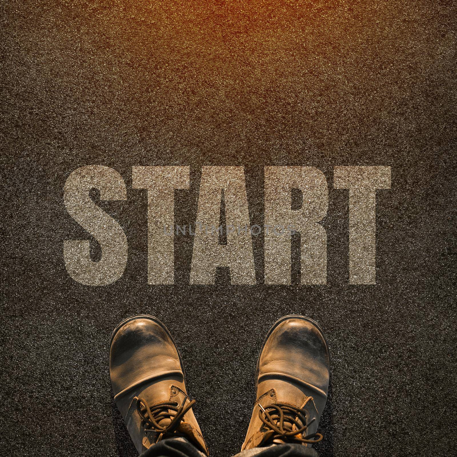 A pair of feet on a tarmac road with white print of the word start for the concept of starting point. Start concept background.