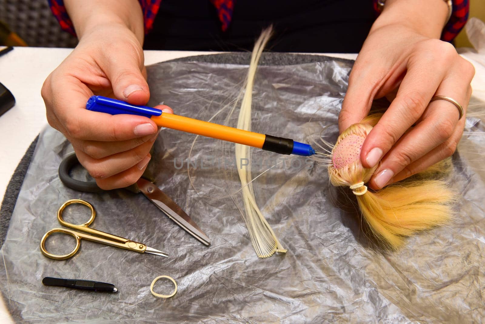 female hands and homemade tool on the table, how to make a hairstyle for a doll, hobby concept.