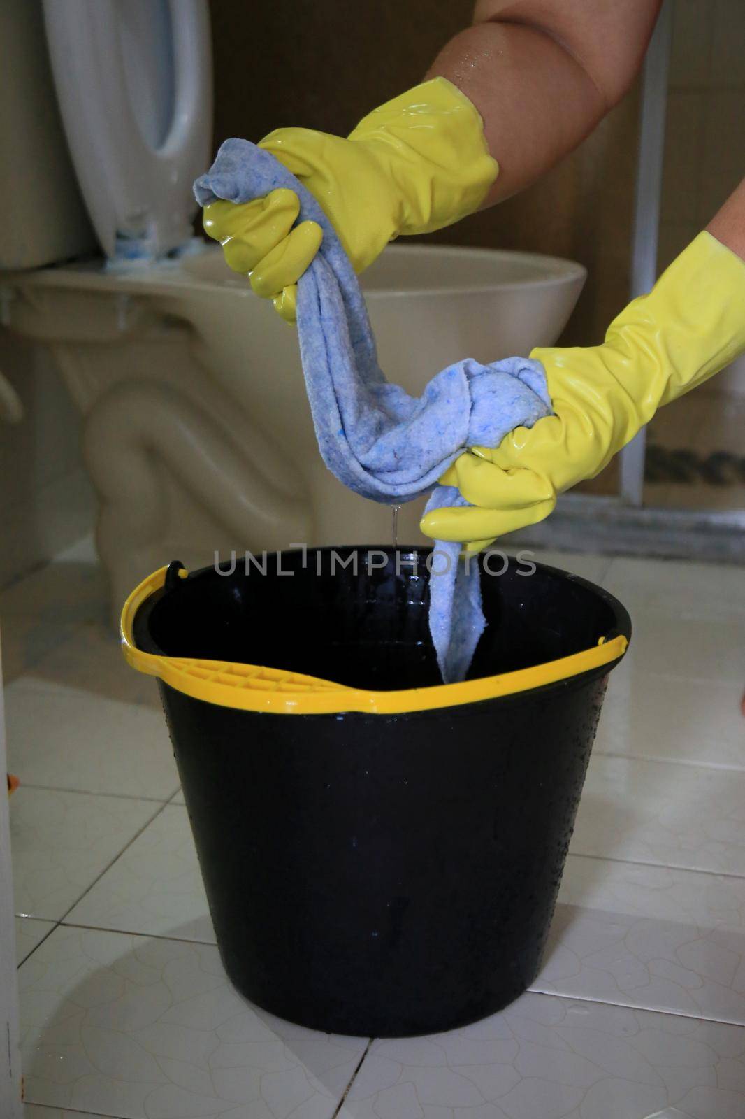 salvador, bahia, brazil - february 21, 2021: person wearing a rubber glove and holding a cloth next to a bucket while cleaning a bathroom in a residence in the city of Salvador.