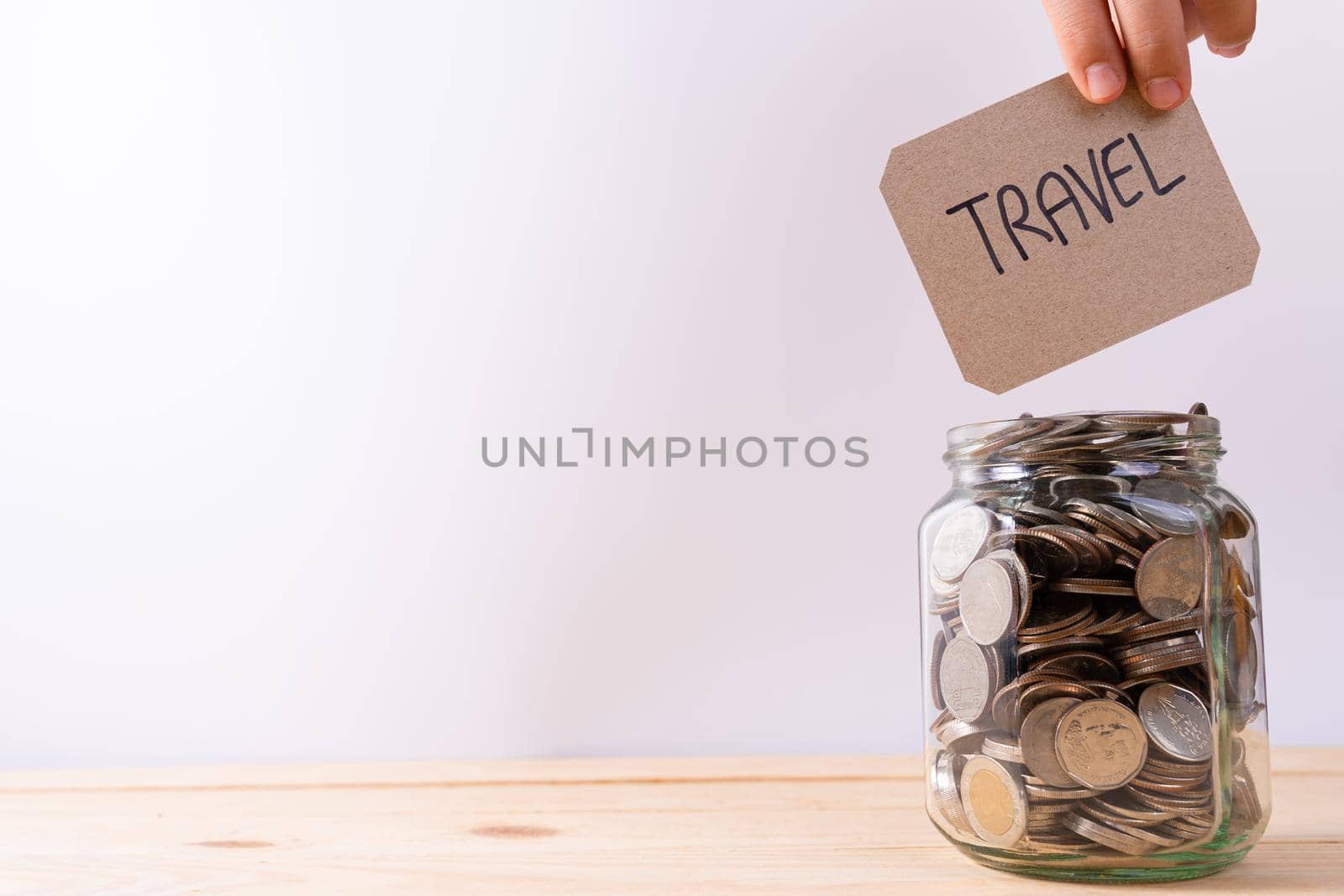 Jar full of coins with travel word paper on wooden table isolated grey background. Saving money and investment concept. by mikesaran