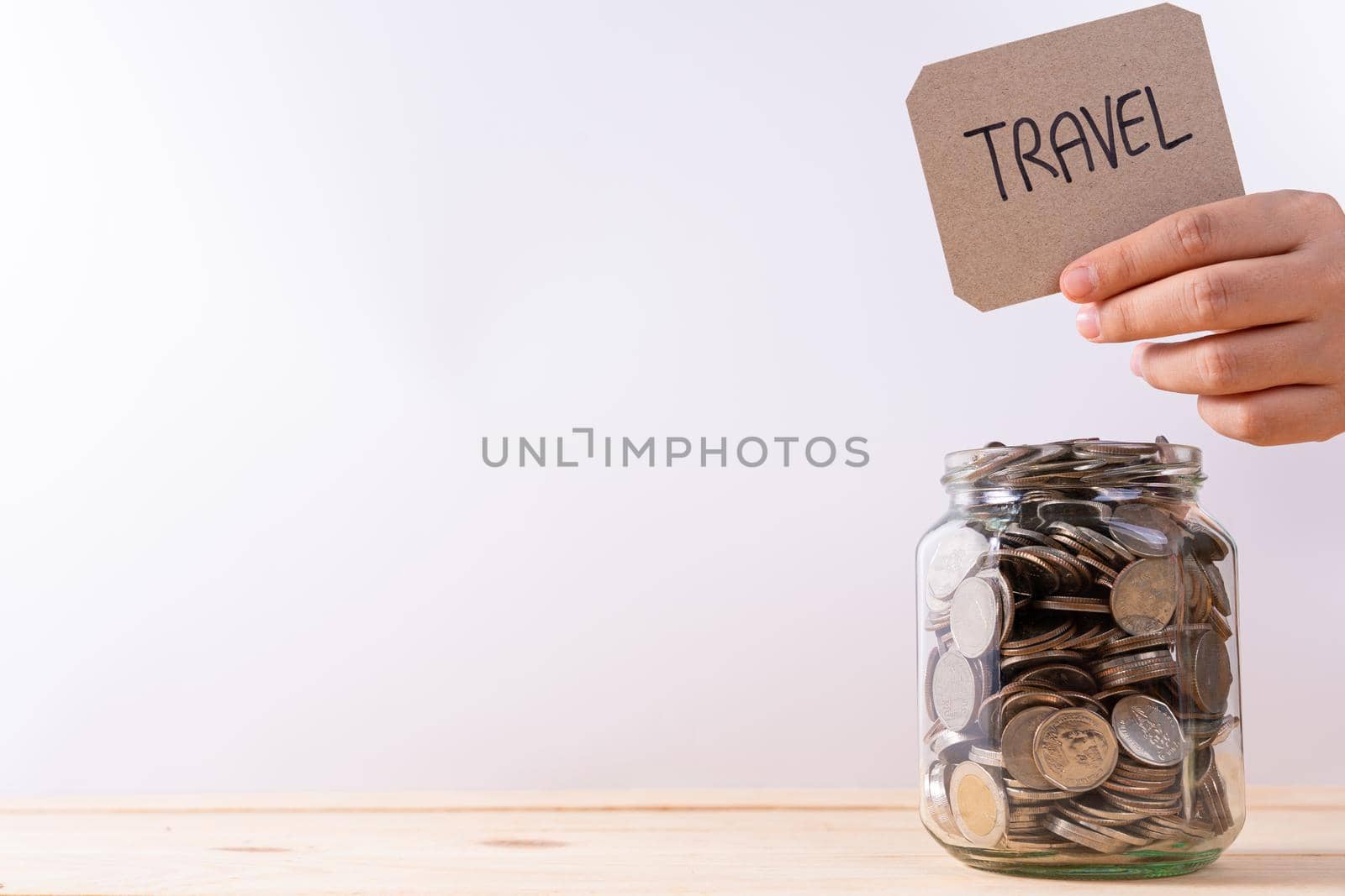 Jar full of coins with travel word paper on wooden table isolated grey background. Saving money and investment concept. by mikesaran