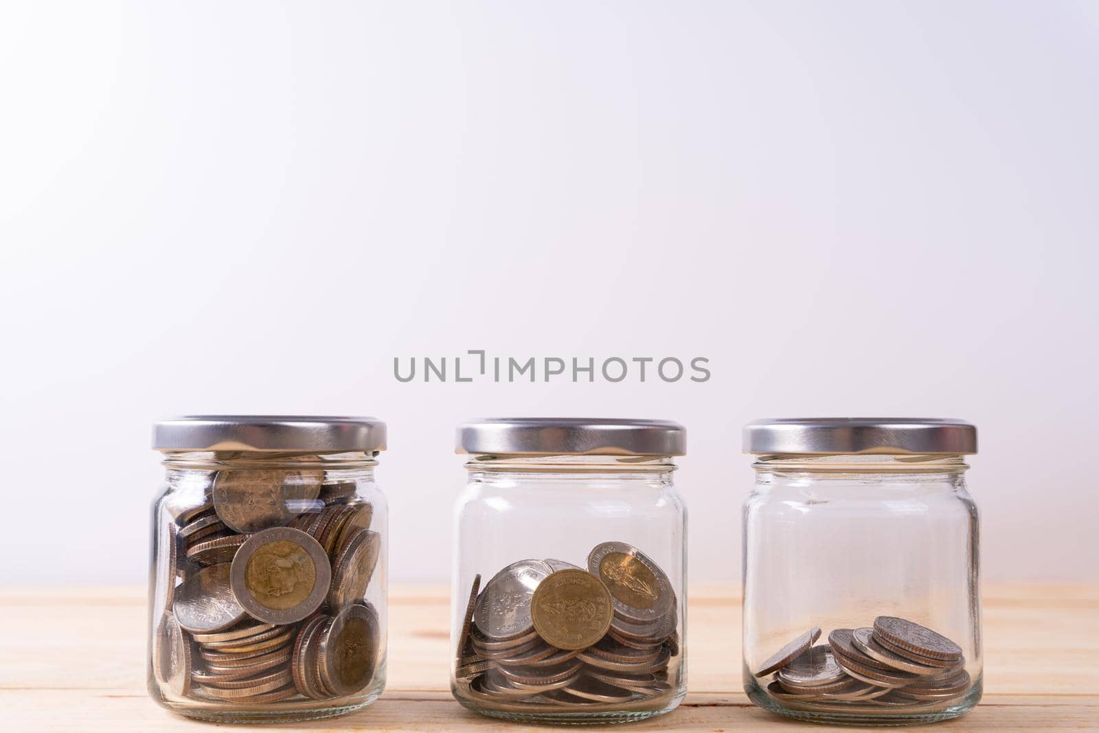 Jar full of coins with different level of coin on wooden table isolated grey background. Saving money and investment concept.