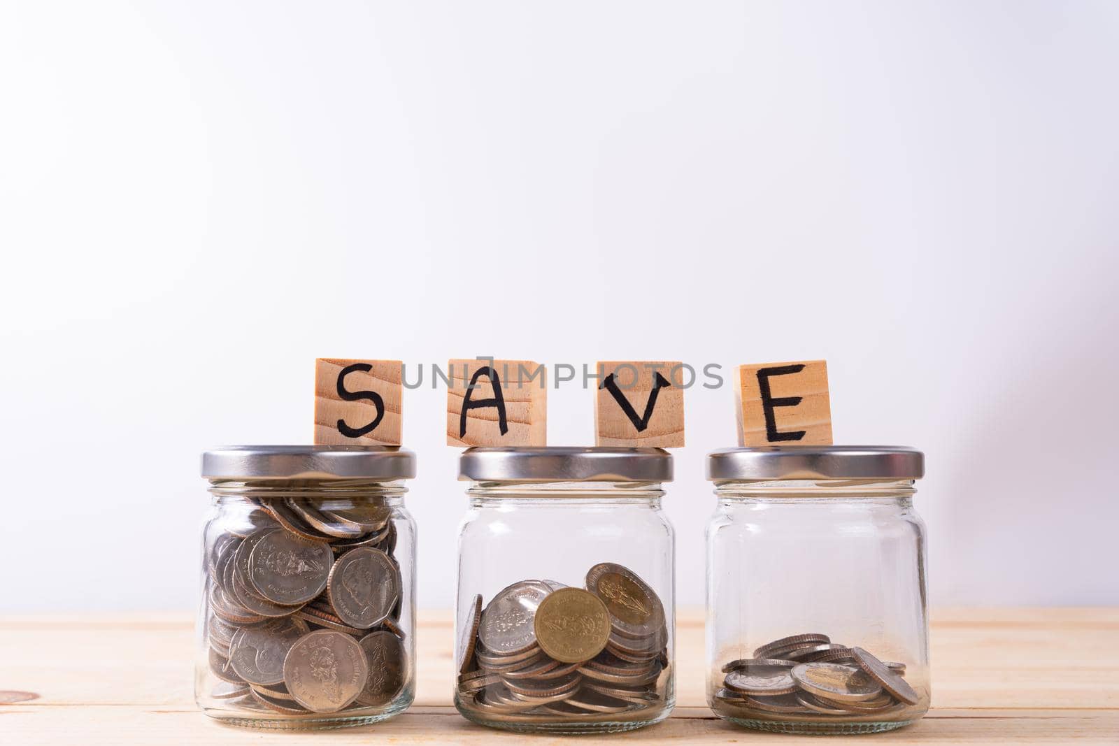 Jar full of coins and wood block with save word on wooden table isolated grey background. Saving money and investment concept.