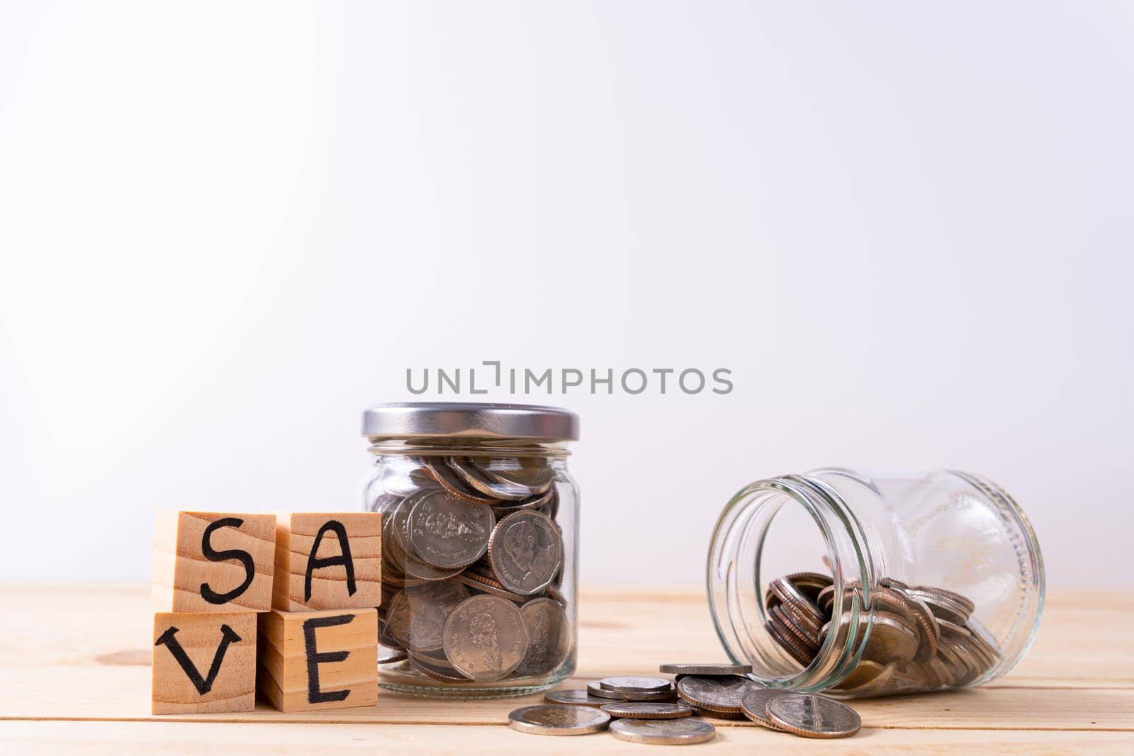Jar full of coins and wood block with save word on wooden table isolated grey background. Saving money and investment concept. by mikesaran