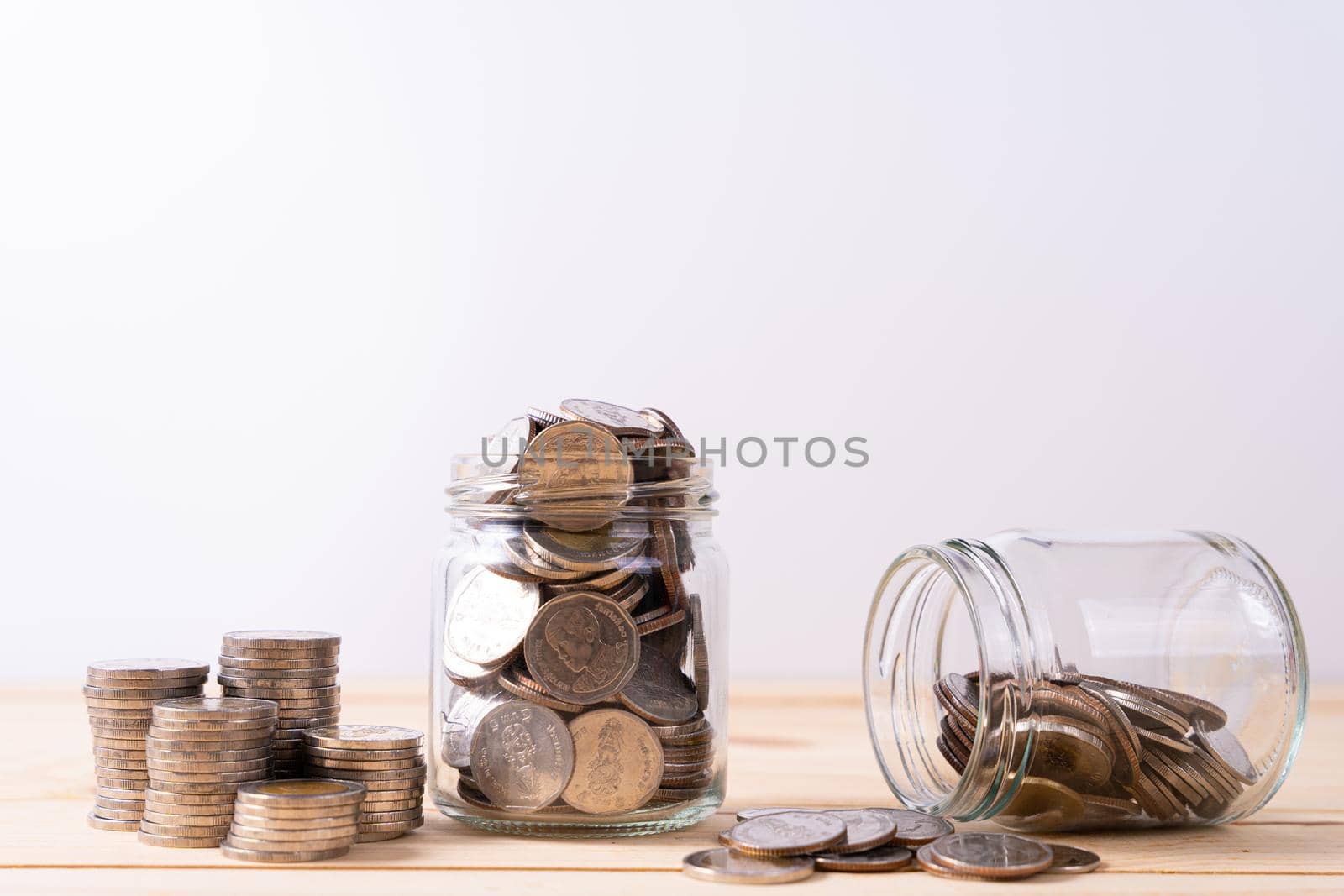 Jar full of coins with stack coin on wooden table isolated grey background. Saving money and investment concept.