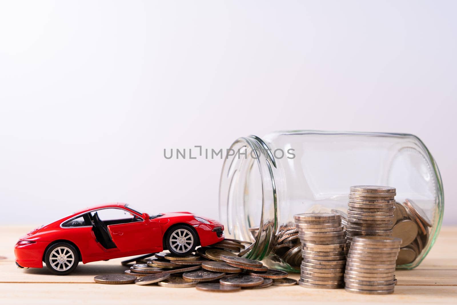 Jar of coins and red car on wooden table isolated grey background. Saving money and investment concept.