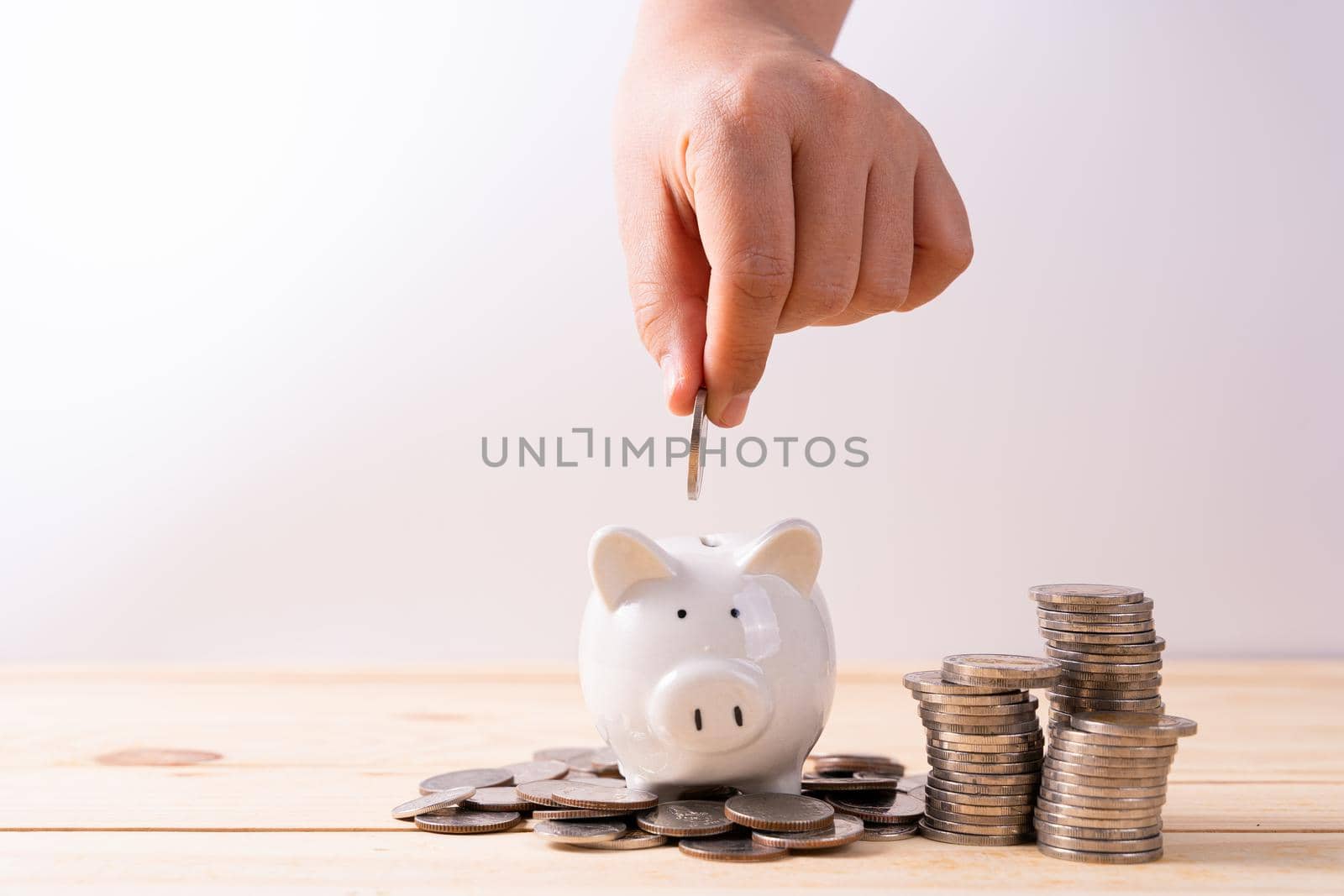 Hand put money coin into piggy bank with stack coin on wooden table isolated grey background. Saving money and investment concept. by mikesaran