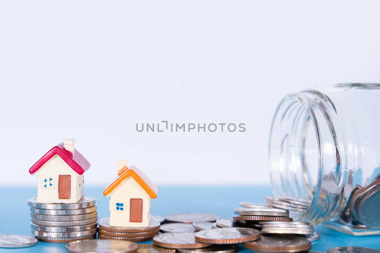 House and coins in jar isolated grey background. Property investment and house mortgage financial concept.