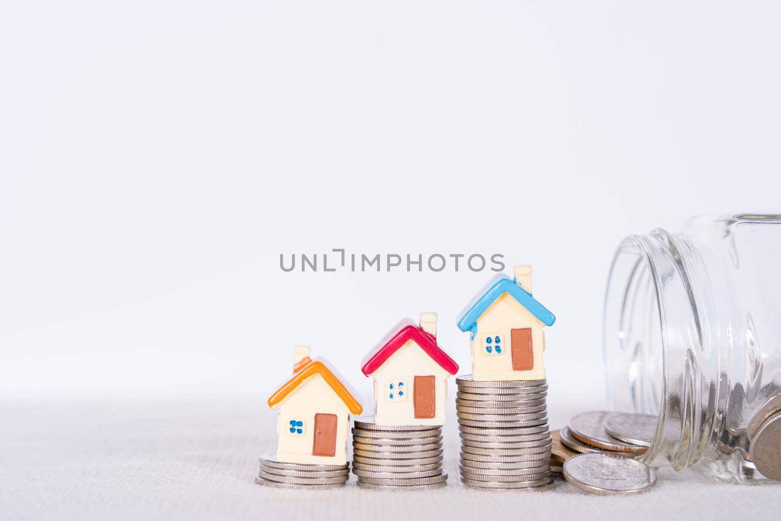 House and coins in jar isolated grey background. Property investment and house mortgage financial concept.