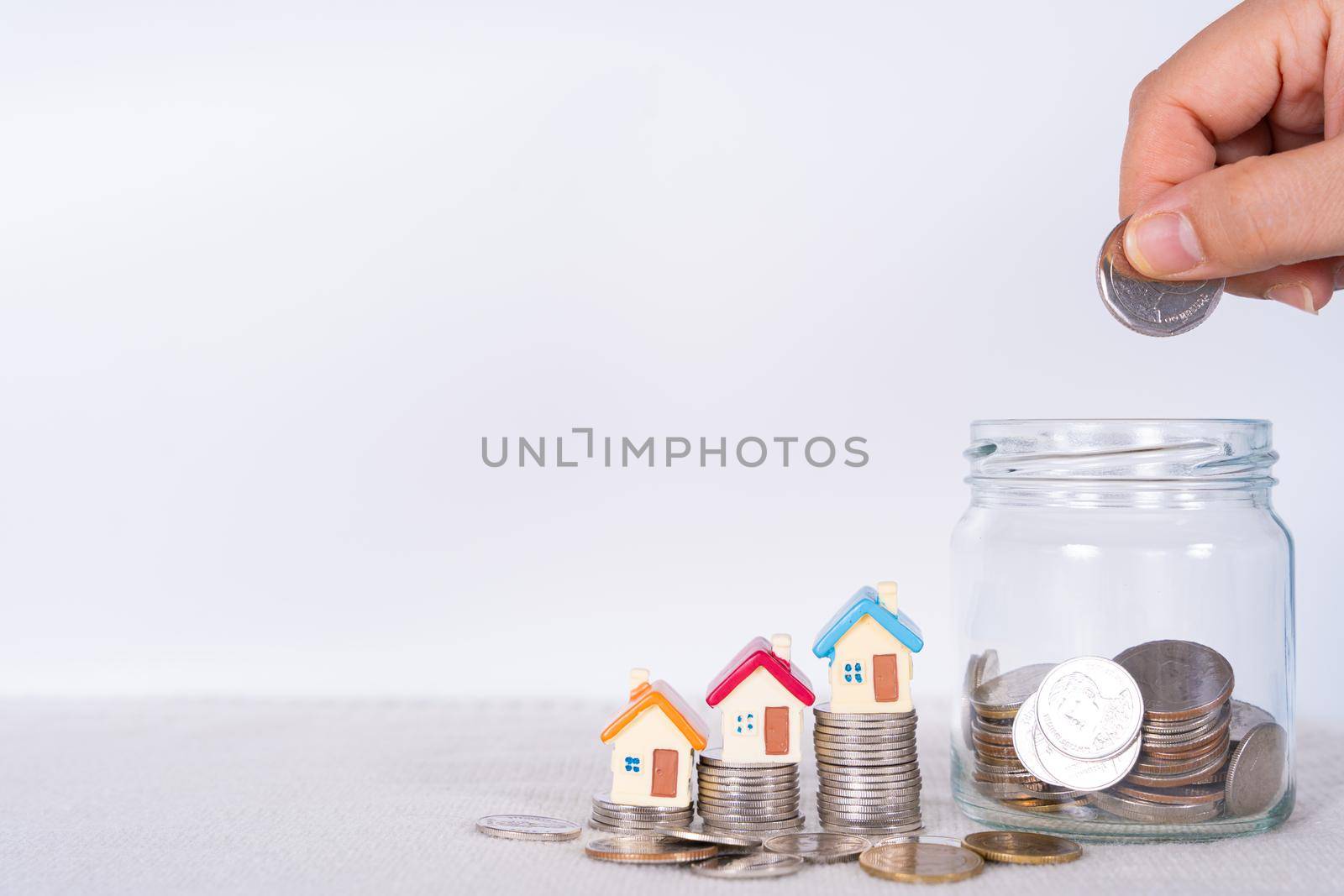 Hand put money coin into jar with house on stack coins isolated grey background. Saving money and investment concept.