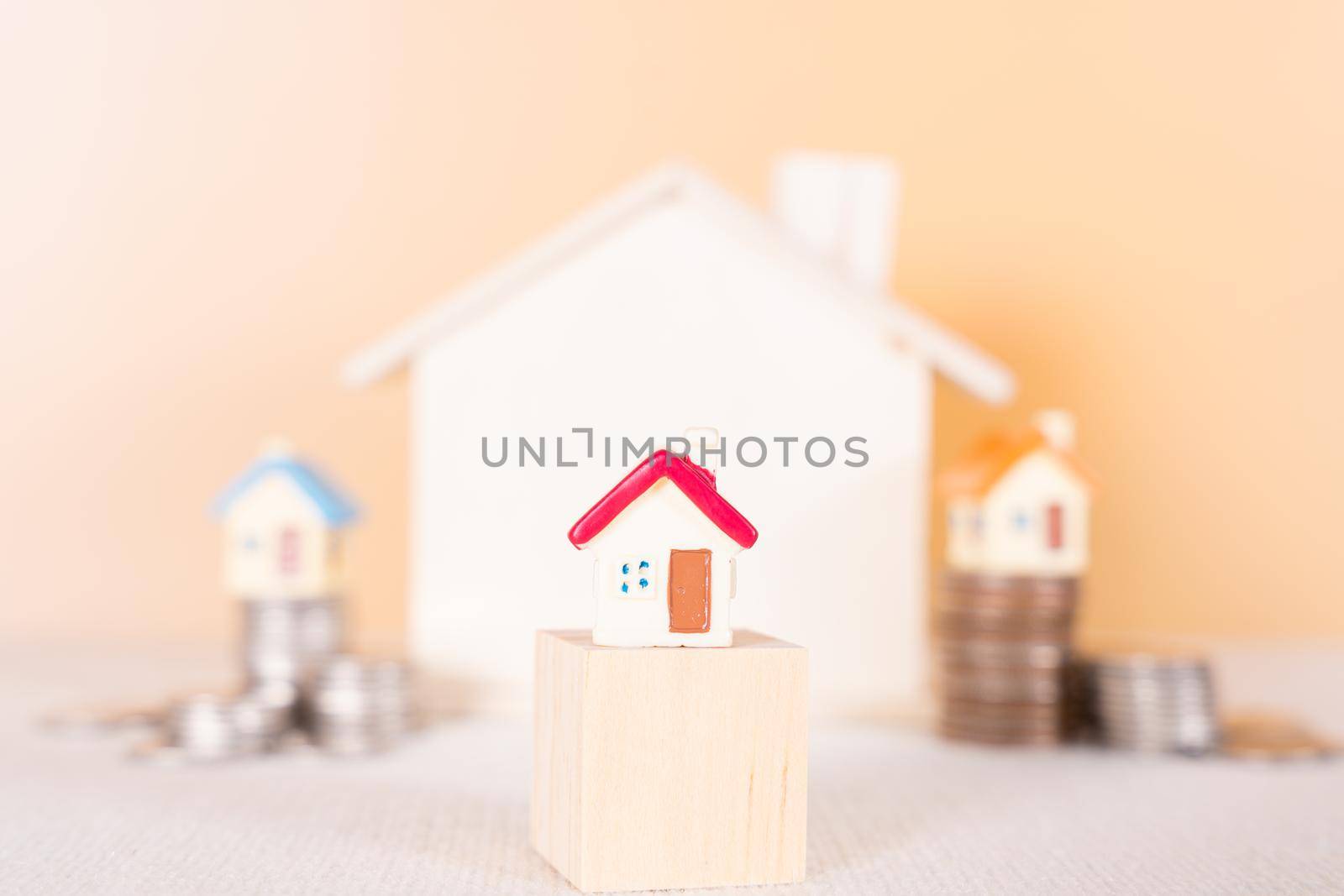 House on wooden block and stack coins isolated orange background. Saving money and investment concept.