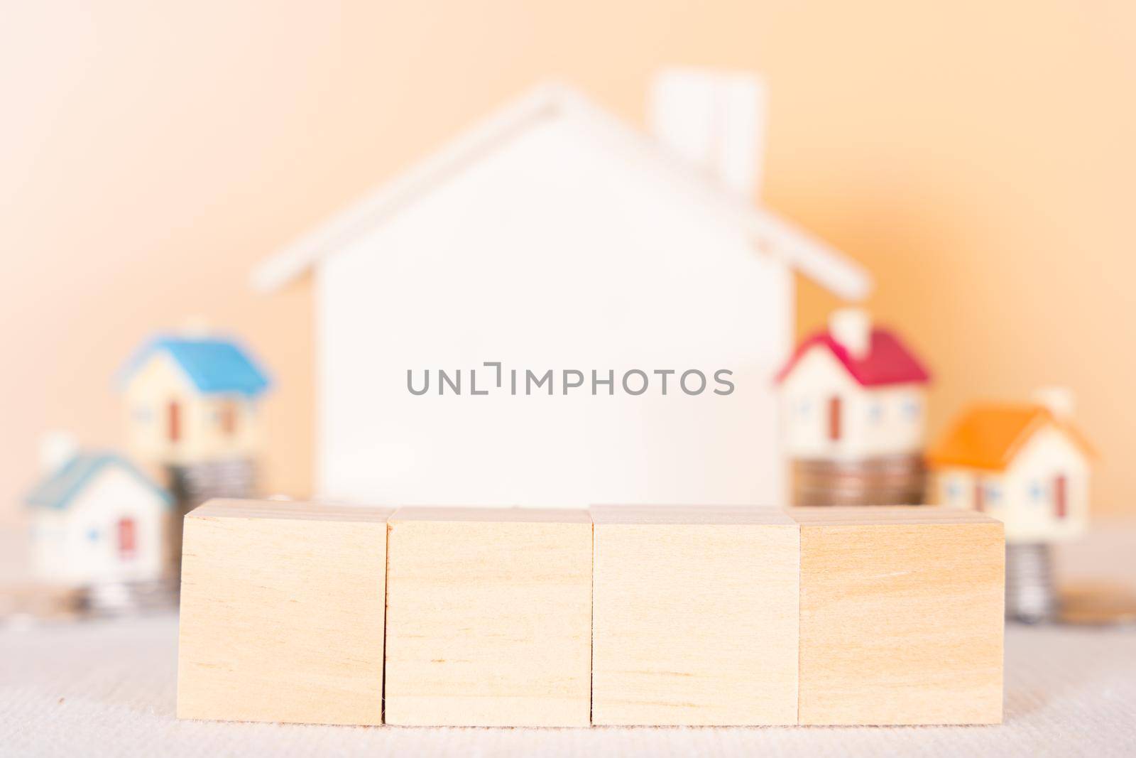 Wooden block and house on stack coins isolated orange background. Saving money and investment concept. by mikesaran