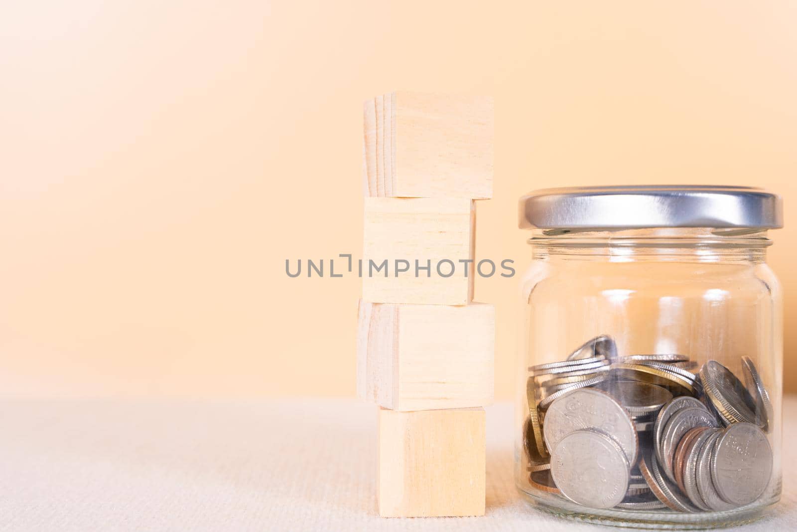Wooden block stack and coin inside jar isolated orange background. Saving money and investment concept.
