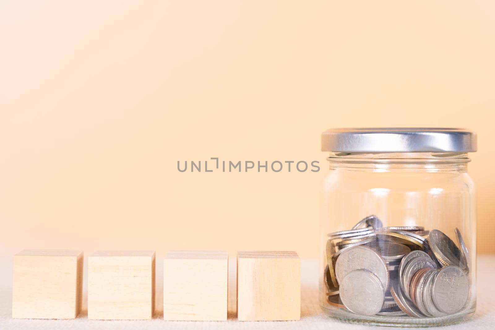 Wooden block and coin inside jar isolated orange background. Saving money and investment concept.