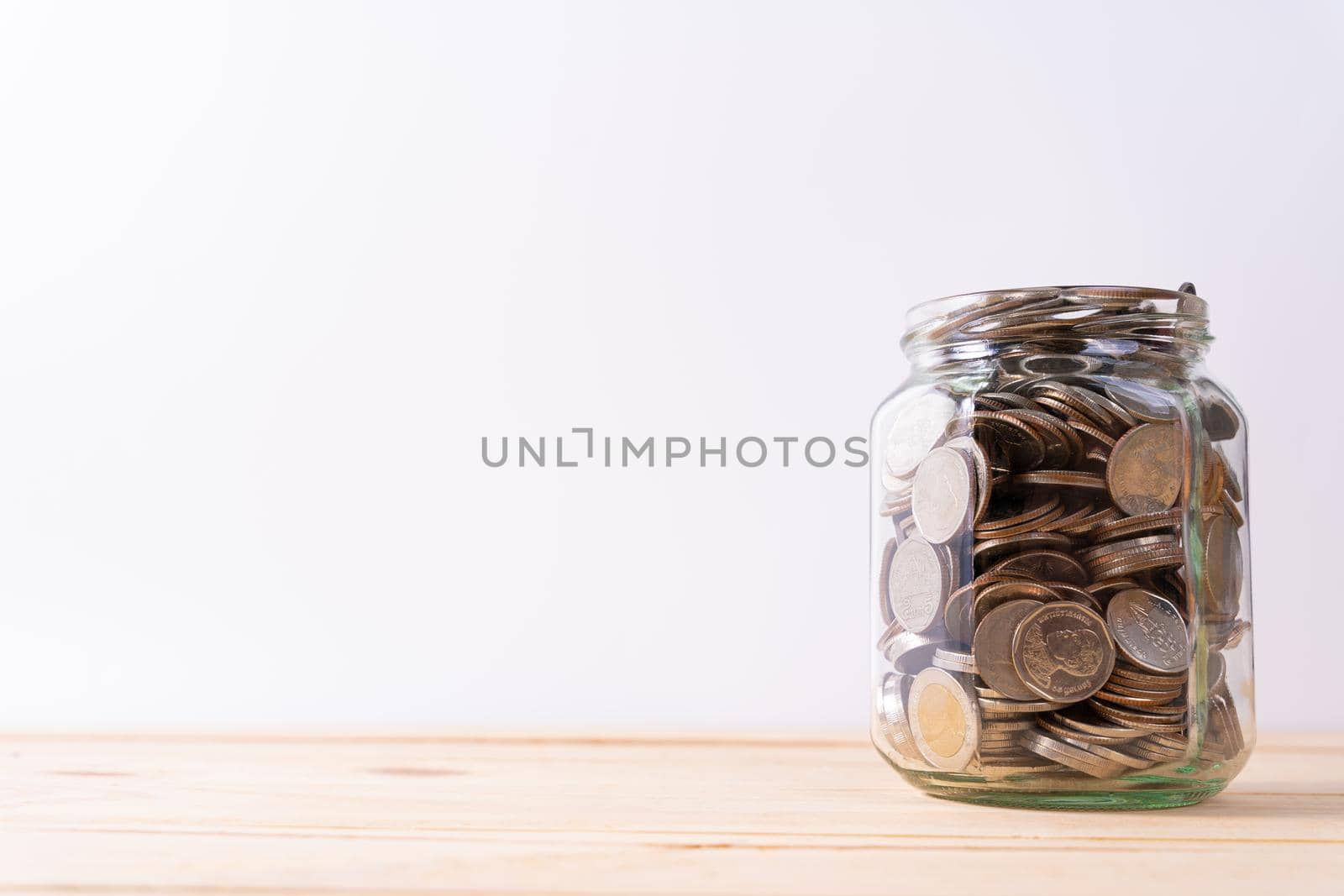 Jar full of coins on wooden table isolated grey background. Saving money and investment concept.