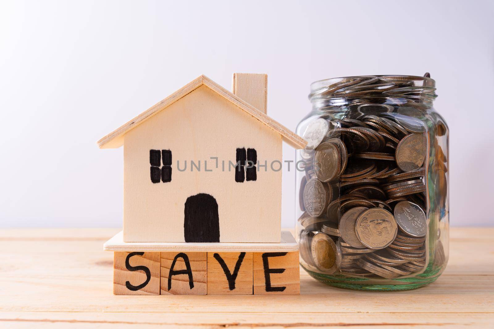 Jar full of coins with save word paper and wooden house on wooden table isolated grey background. Saving money and investment concept. by mikesaran