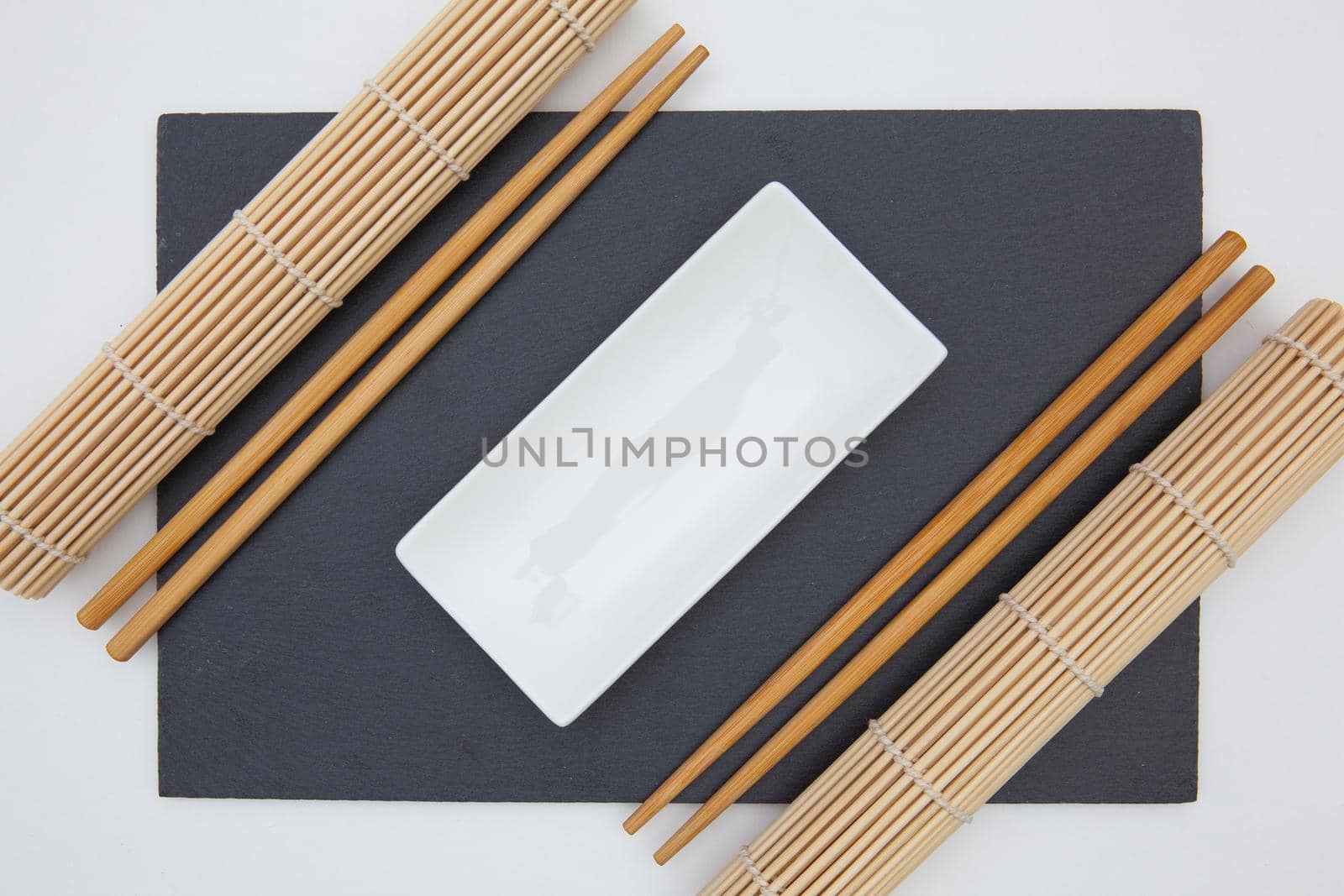 Rectangular slate plate with chopsticks, ceramic plate, bamboo mat for sushi on the white table. by CaptureLight